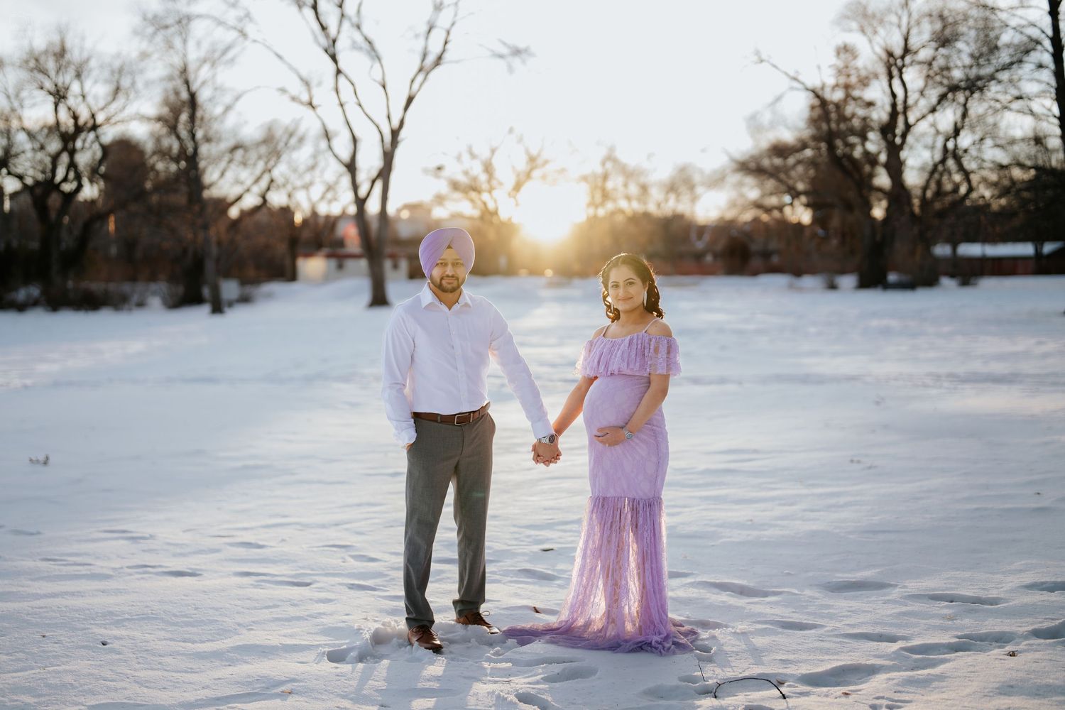 A couple stands together in a snowy landscape with winter sunlight behind them.