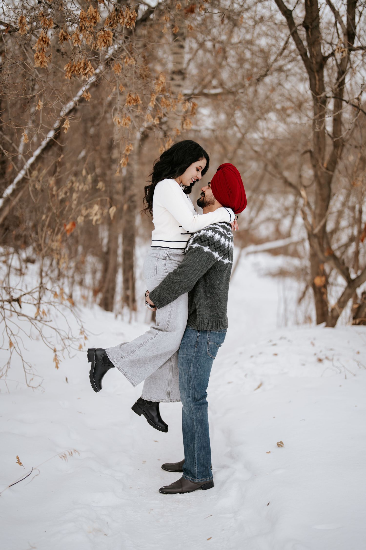 Couple sharing an intimate embrace while standing in a snowy winter forest landscape.