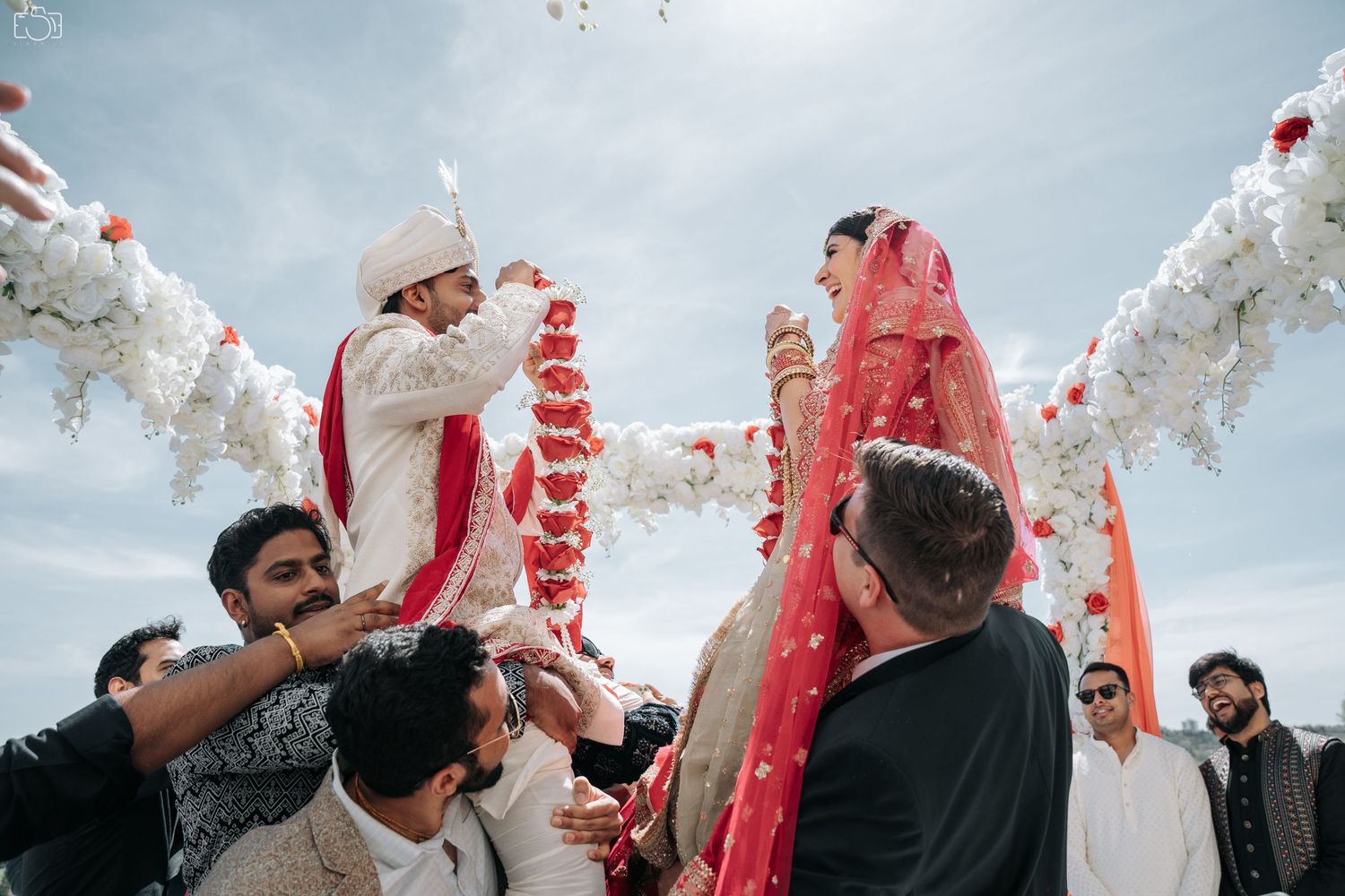 A traditional Indian wedding ceremony with vibrant red garlands against a cloudy sky.