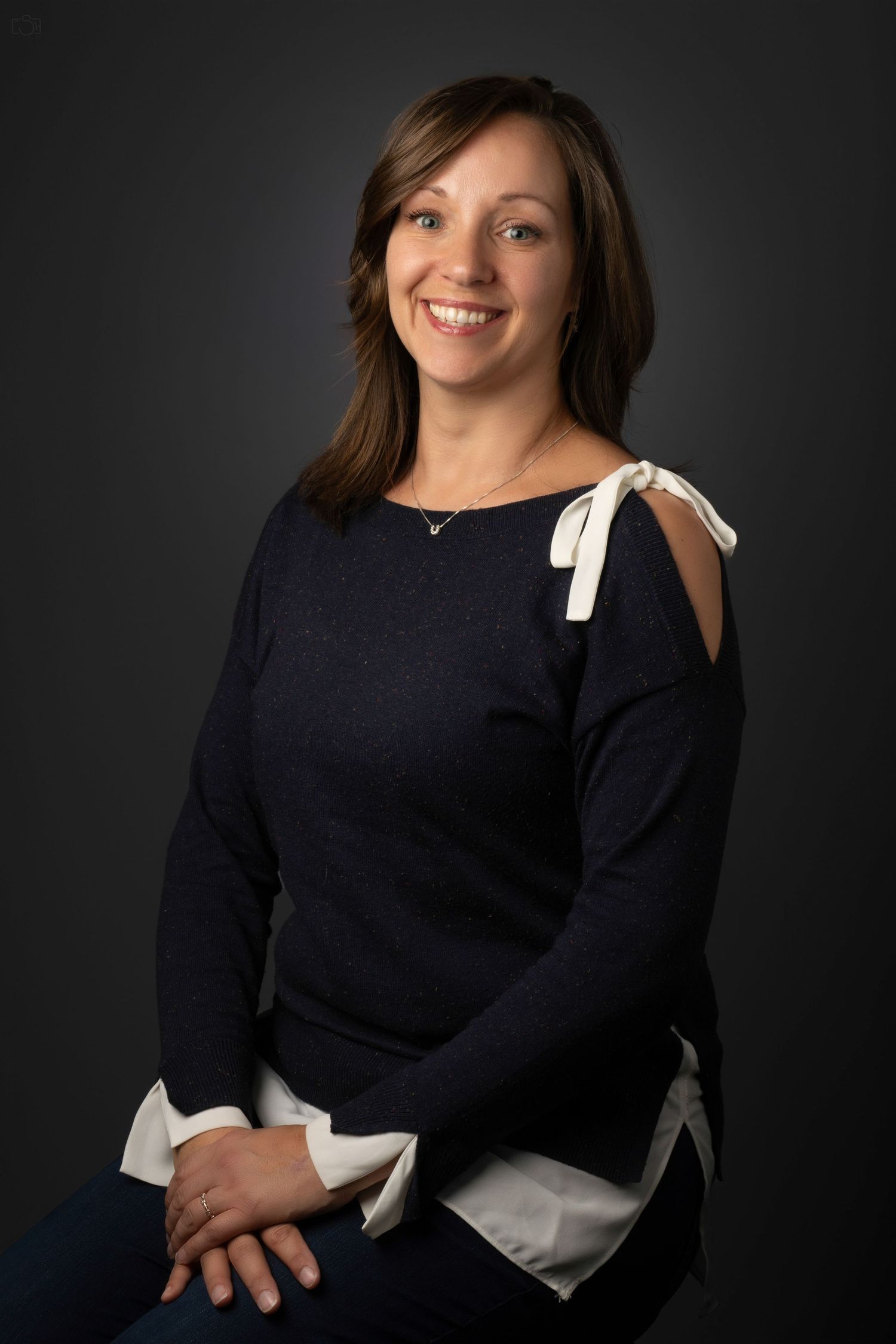 Studio portrait of a person in a navy sweater with white bow detail on the shoulder.