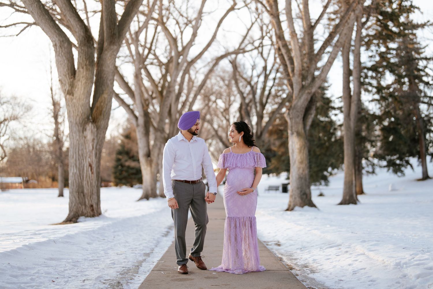 A couple walks together along a snowy path lined with bare winter trees.