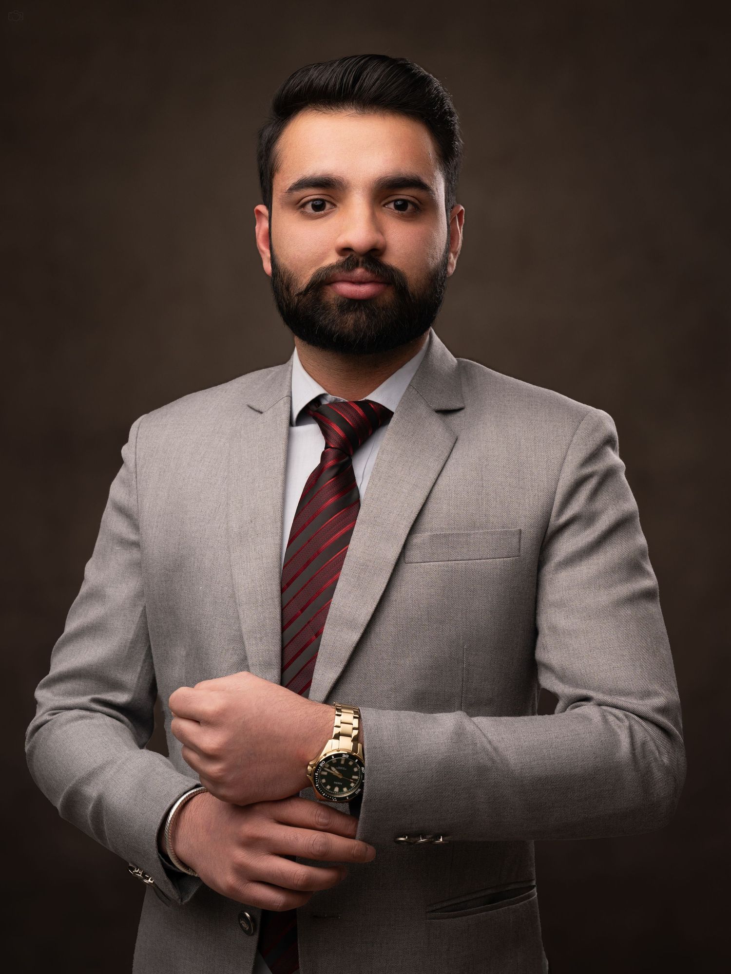 Corporate headshot of a man in grey suit and striped tie against dark background.