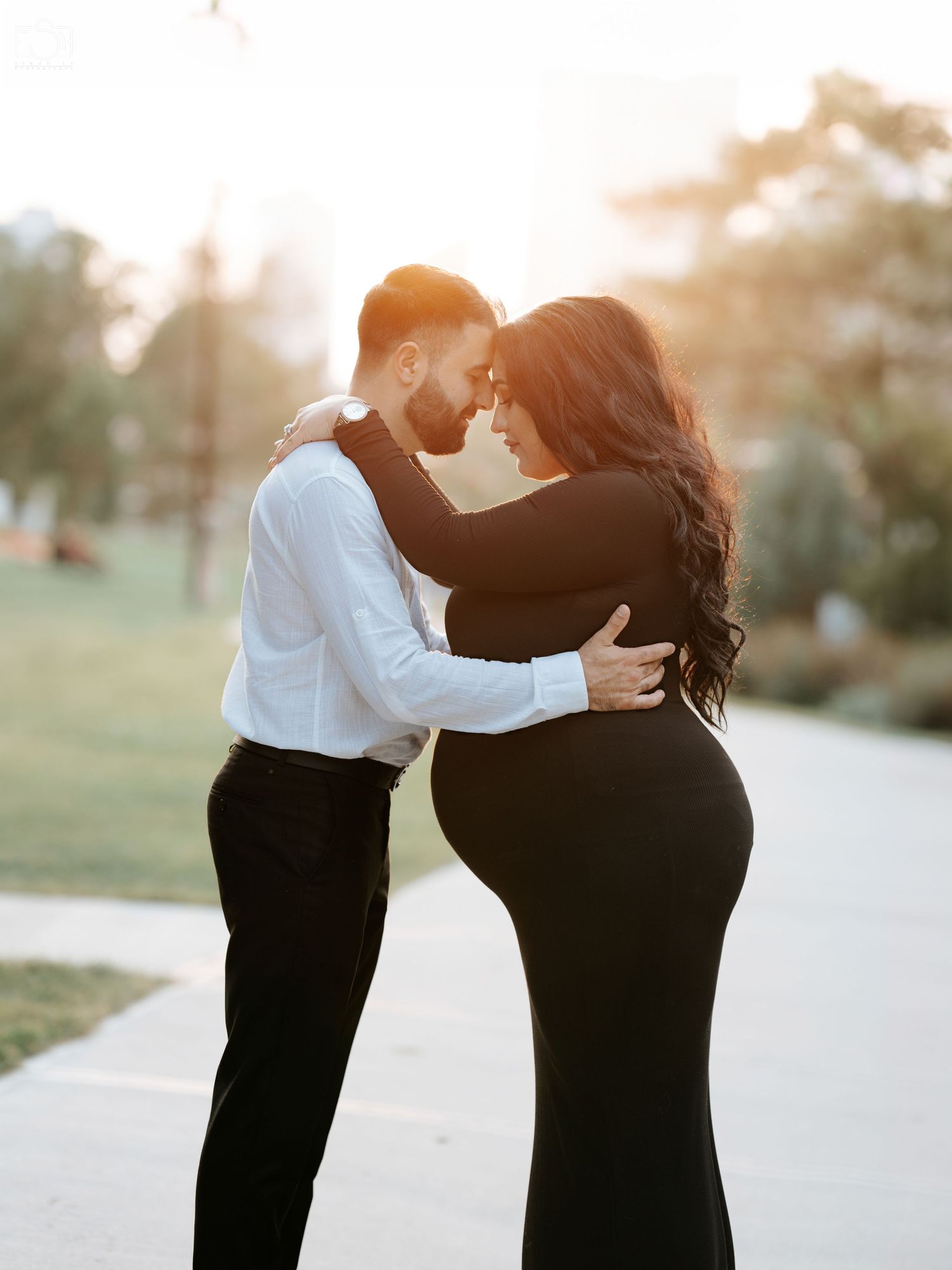 Intimate couple in formal wear embracing during golden hour in a park setting.