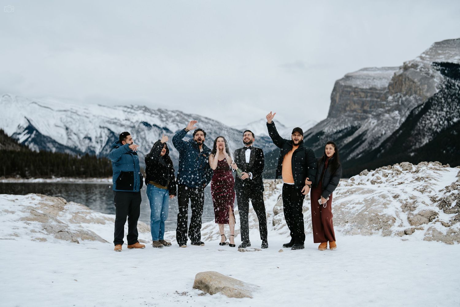Group of friends posing together in winter against snowy mountain backdrop.