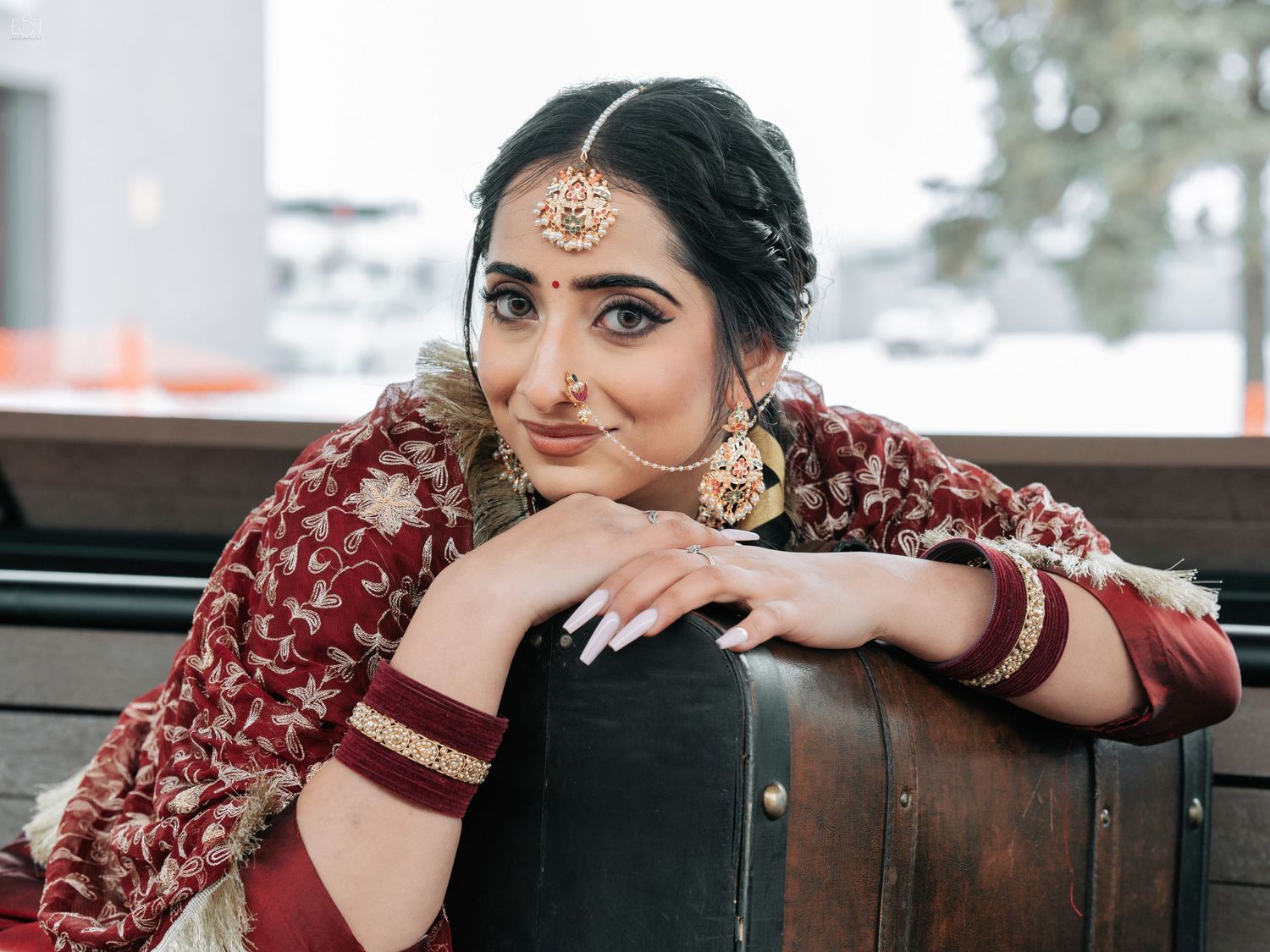 Traditional Indian bride in red lehenga poses elegantly against wooden backdrop.