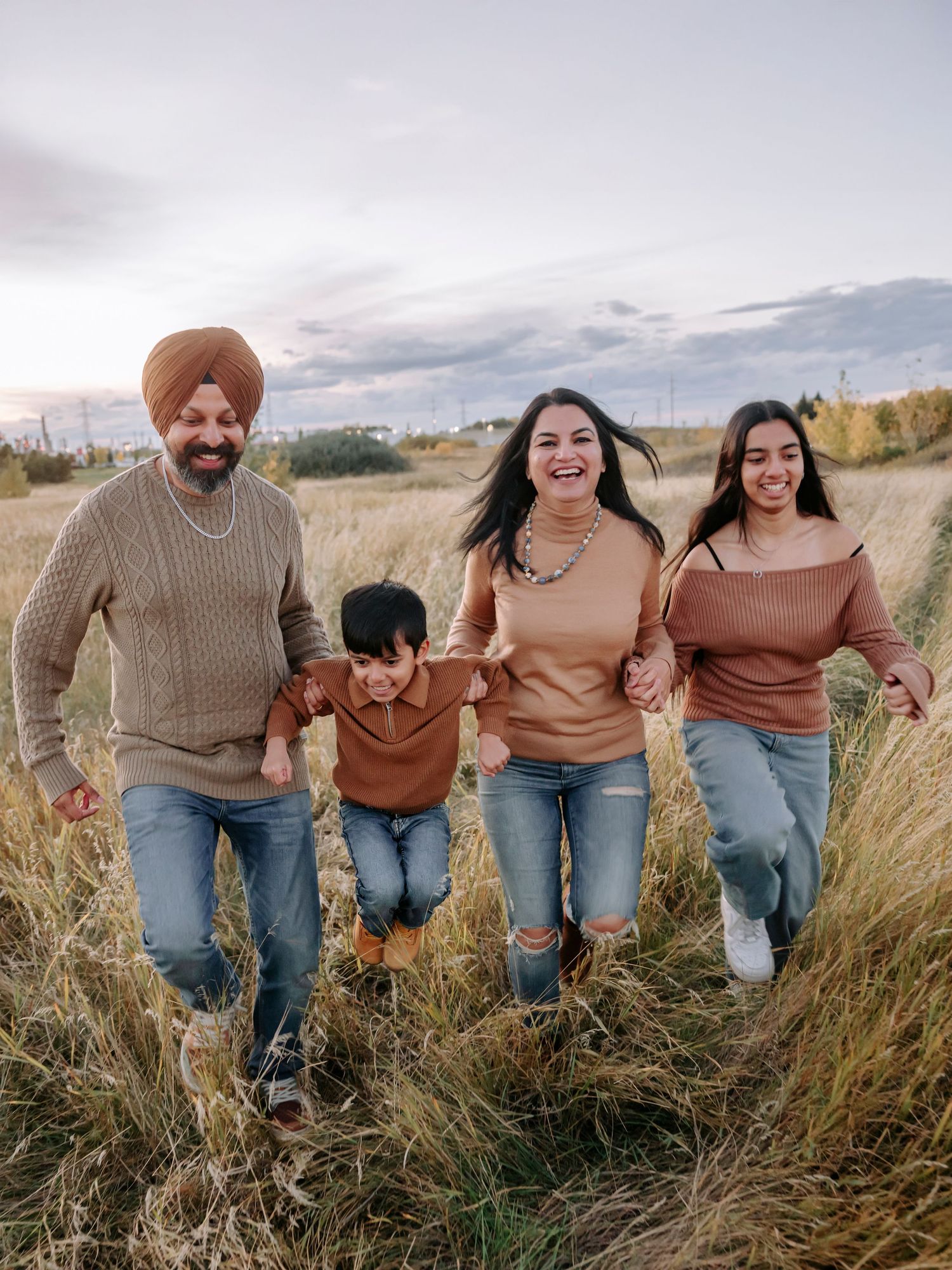 A family runs happily together through a field of tall grass during golden hour under a cloudy sky.