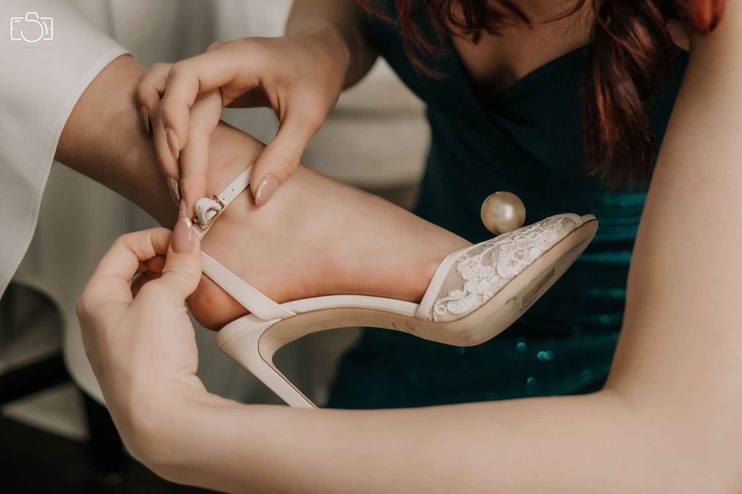 Close-up of hands fastening elegant white bridal heel shoe during wedding preparations.