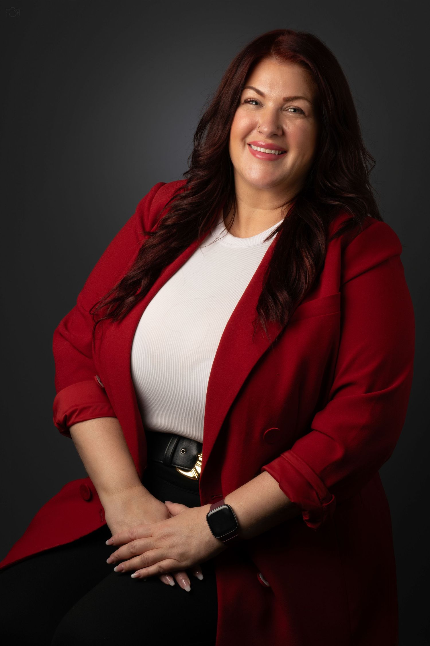 Professional studio portrait featuring a woman in a red blazer and white top against a dark background.