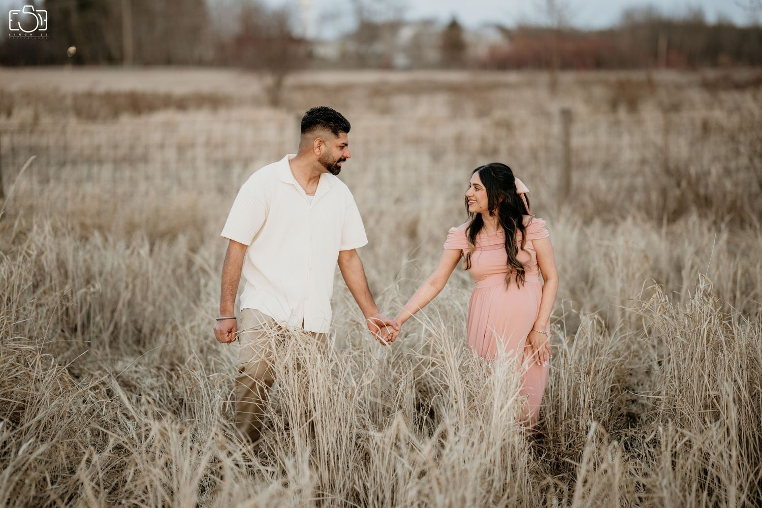 A couple holds hands in a field of tall grass during golden hour.