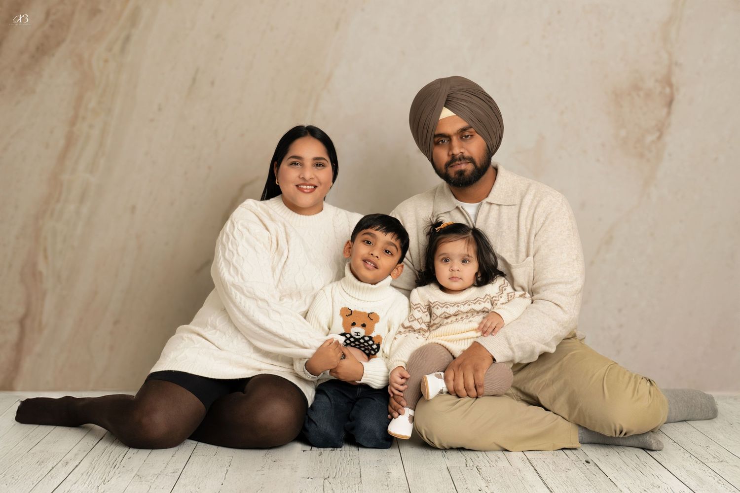 Family portrait of parents and two children wearing matching cream sweaters on white background.
