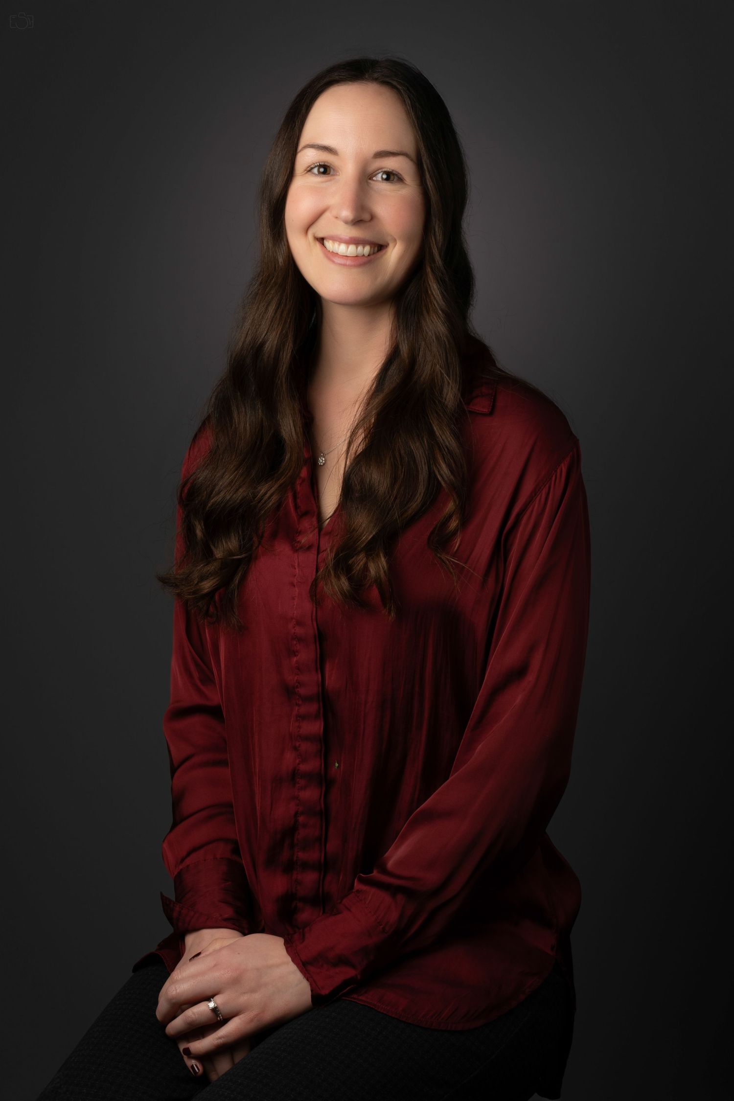 Professional studio portrait of a woman in a burgundy silk blouse against a dark background.