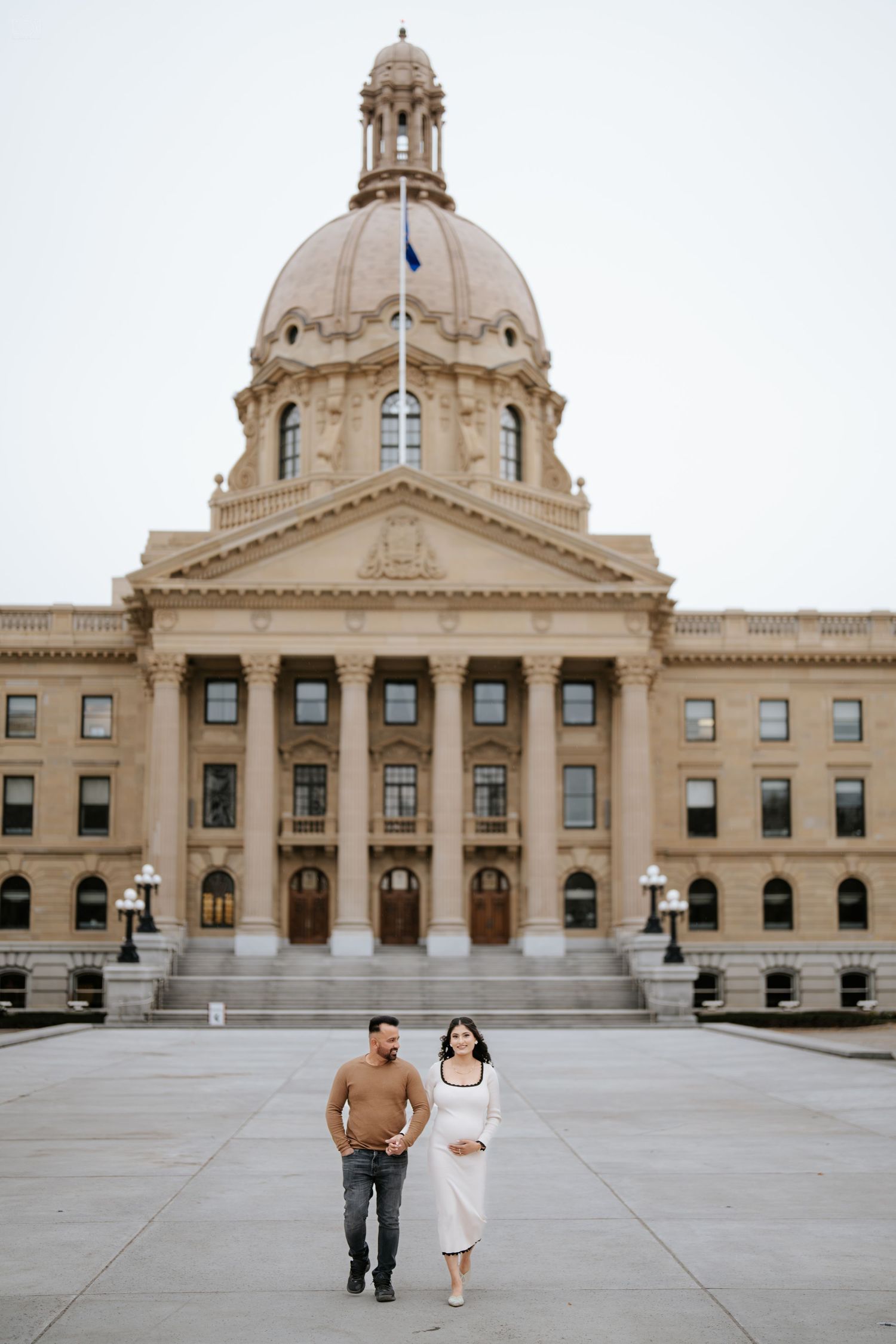 Couple walking in front of Alberta Legislative Building with its iconic domed architecture.