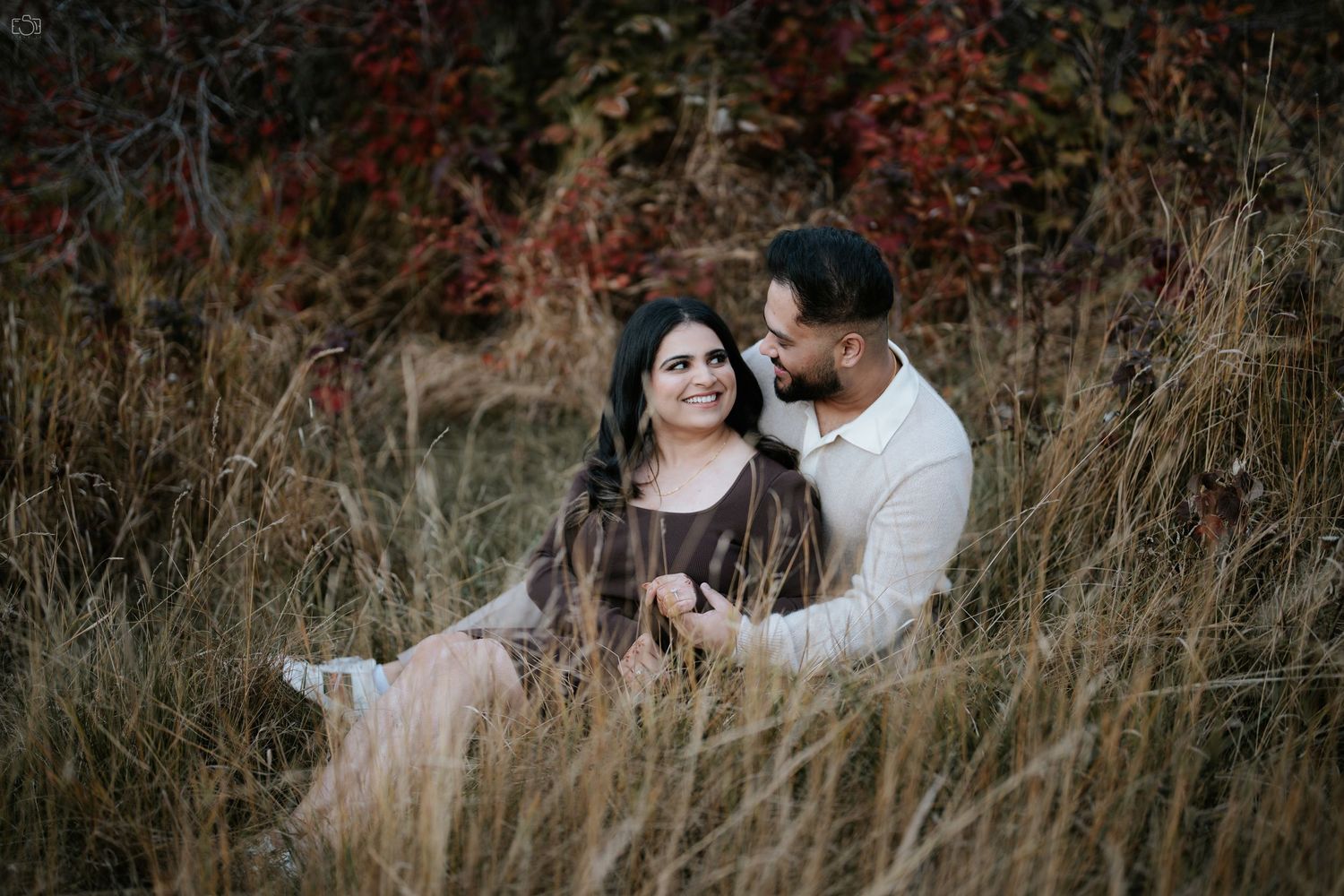 Couple sits intimately in tall grass during moody outdoor photoshoot.
