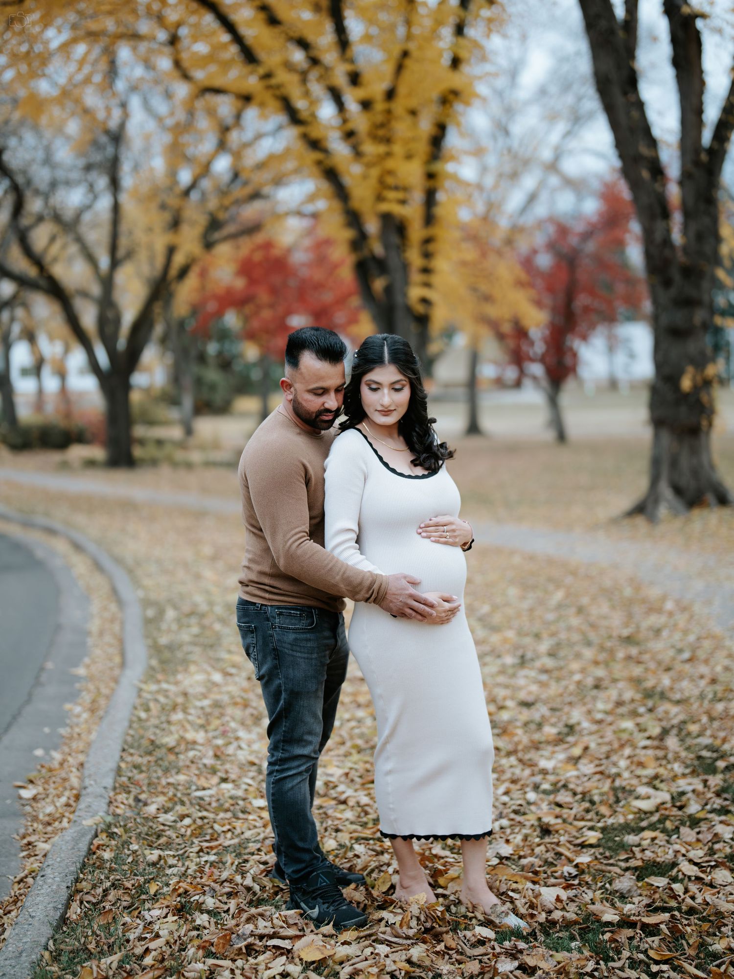 A maternity photo in autumn with yellow and red trees in the background.