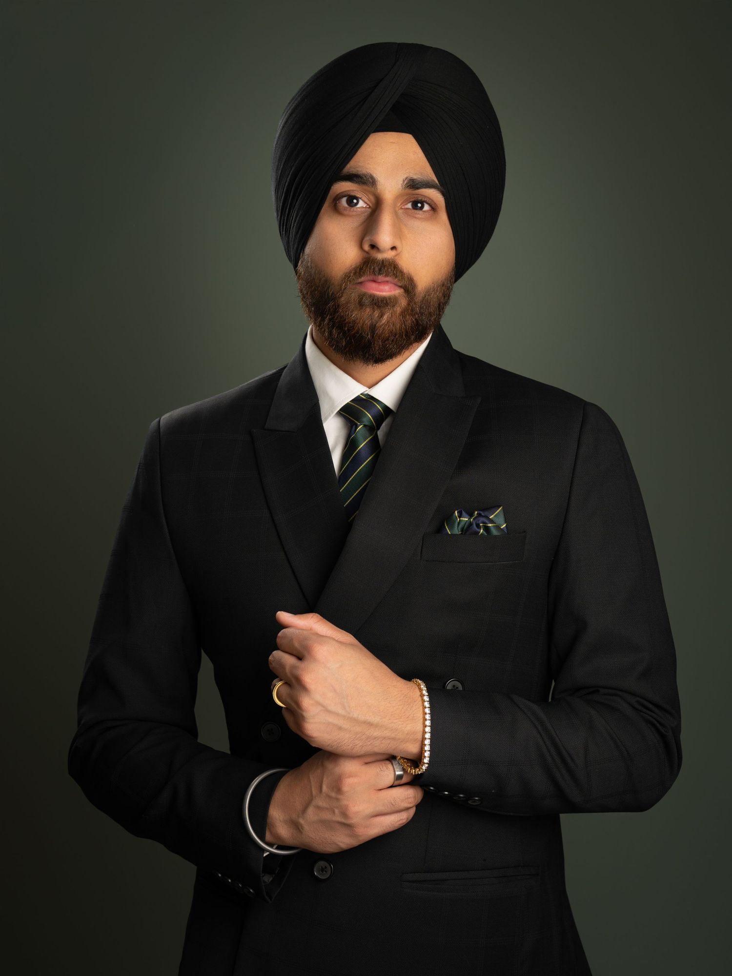 Professional portrait of a person in a black suit and turban with a striped tie.