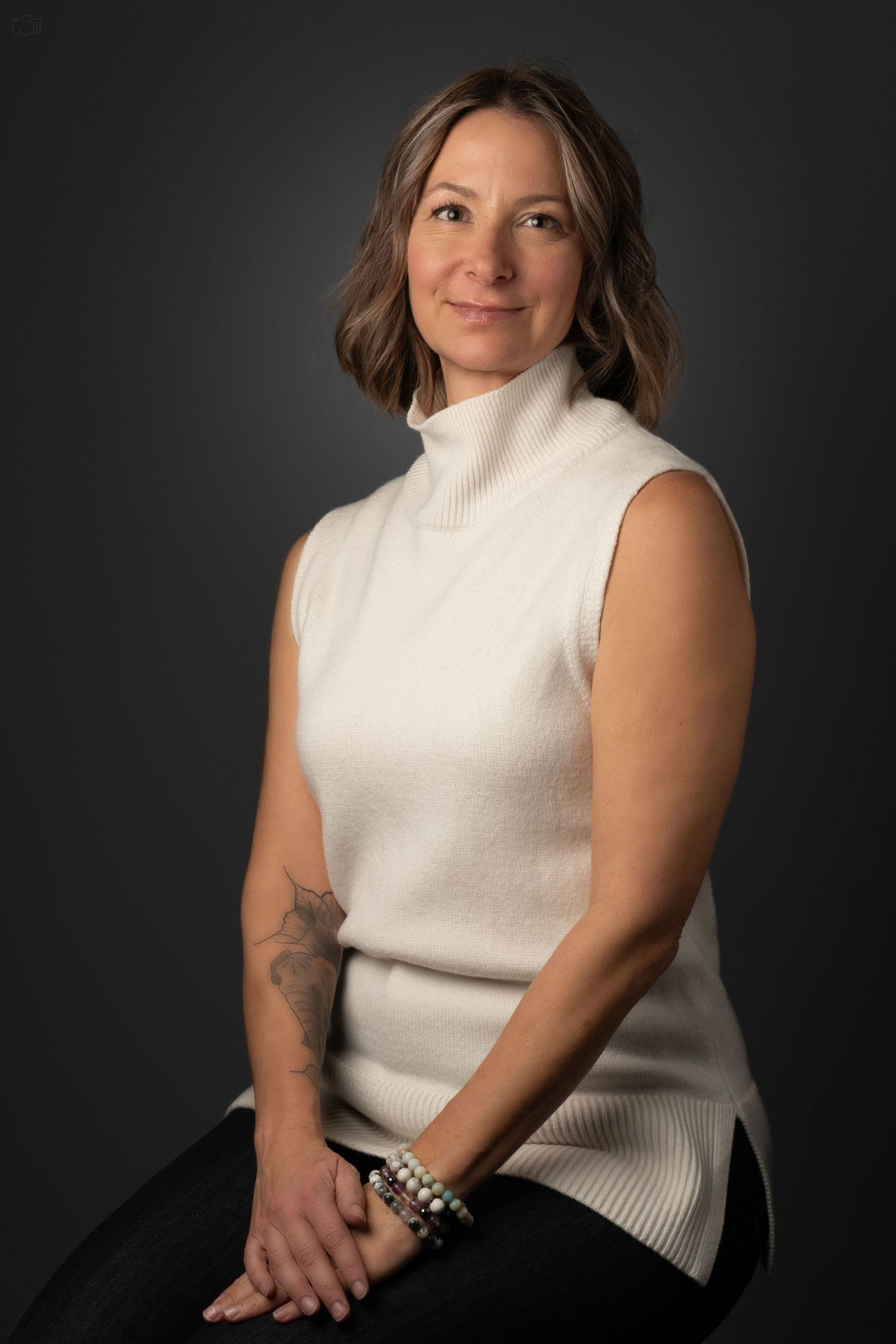 Professional portrait of a person in a white sleeveless turtleneck sweater against a dark backdrop.