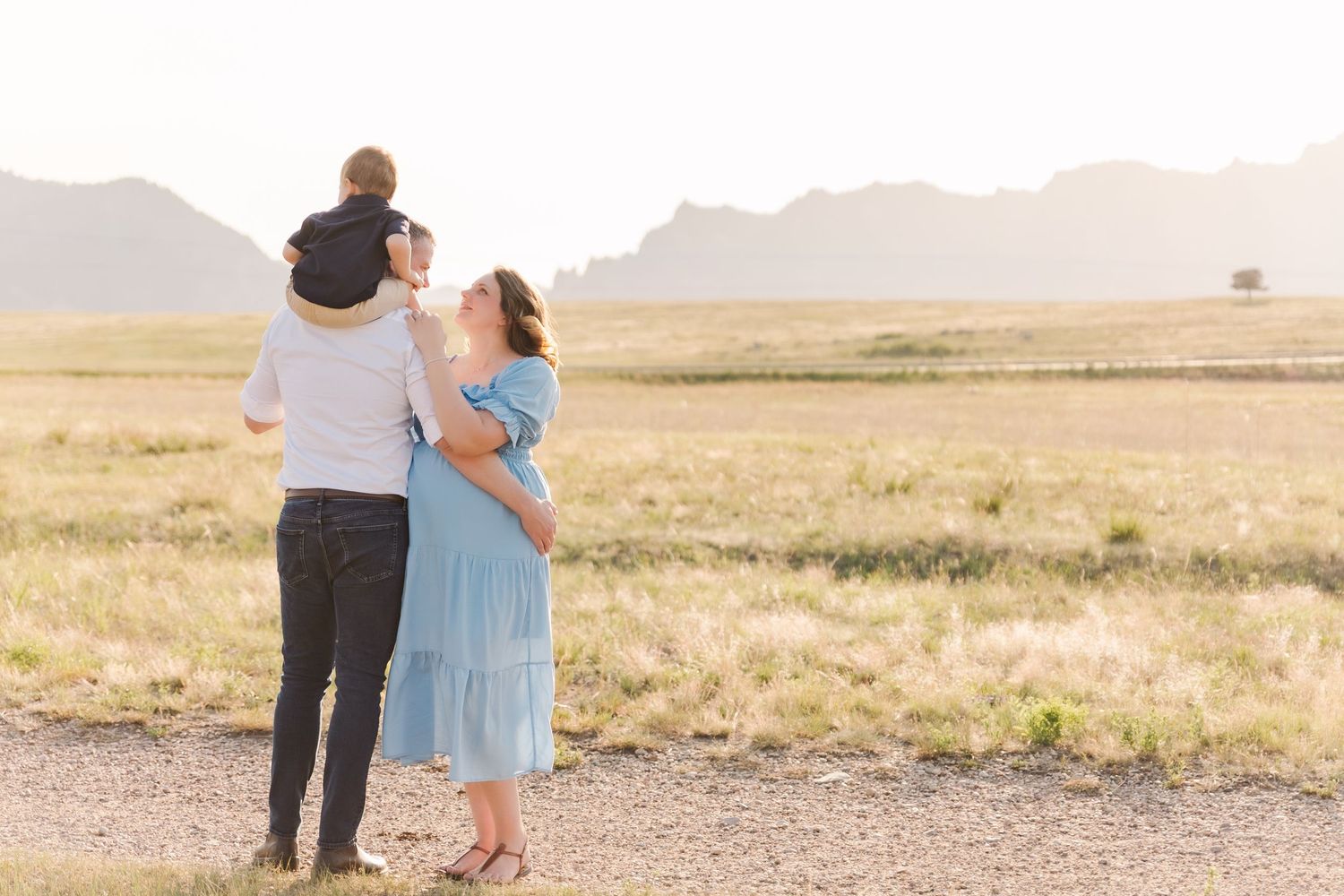 Family of three enjoying a sunny day in an open field with mountain views in the background.