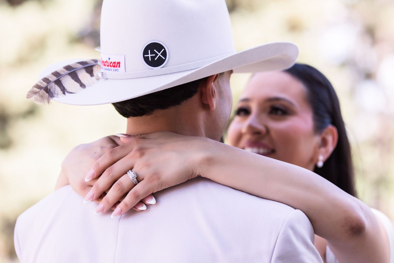 Bride places her hand on groom's shoulder showing diamond ring as he wears a white cowboy hat.