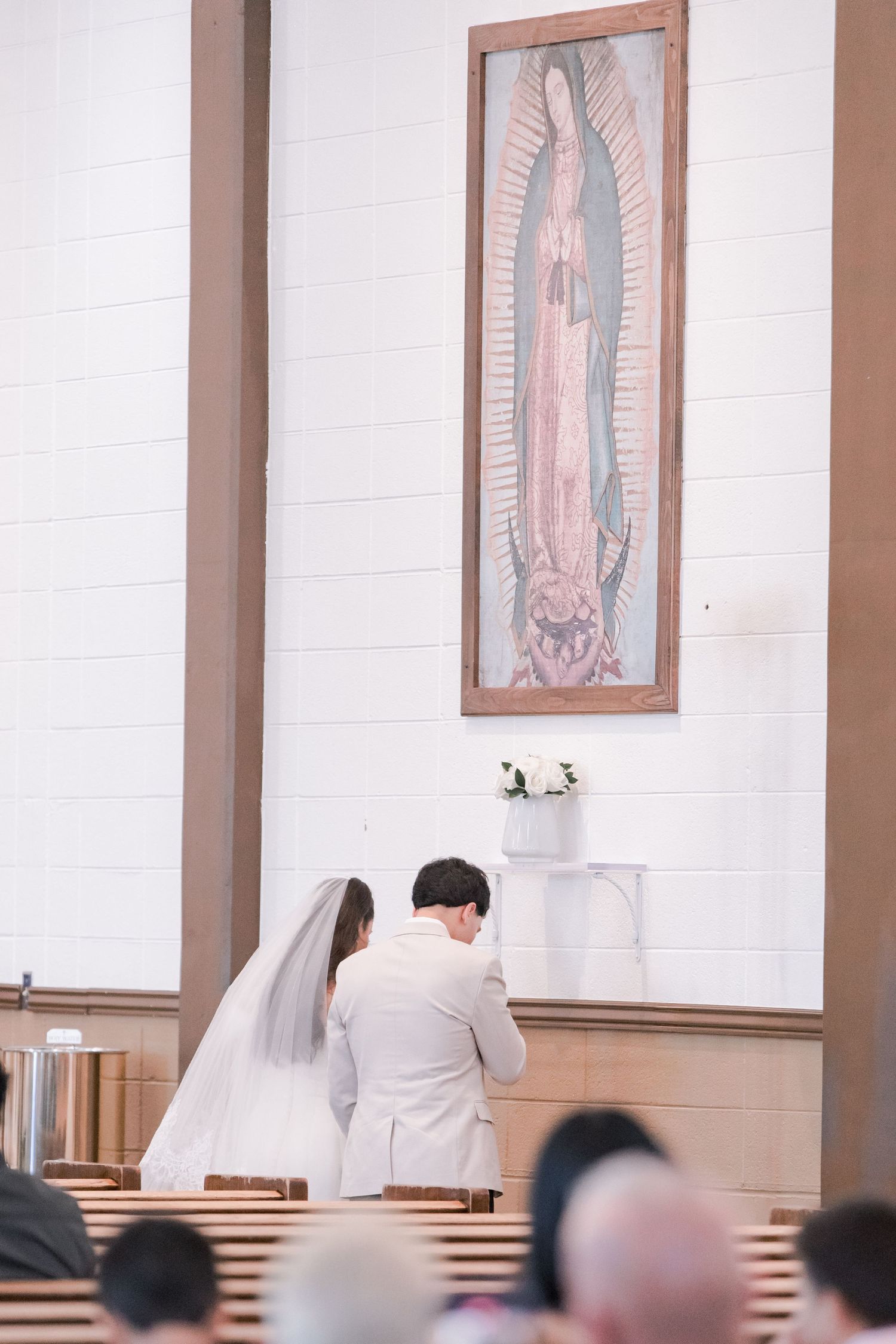 Bride and groom pray together before image of Our Lady of Guadalupe during Catholic wedding ceremony.
