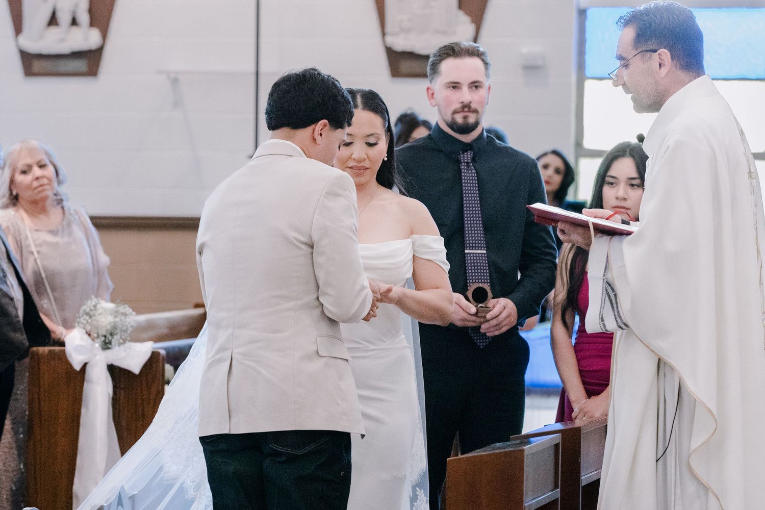 Bride and groom exchange vows at the altar during a Catholic church wedding ceremony with priest officiating.