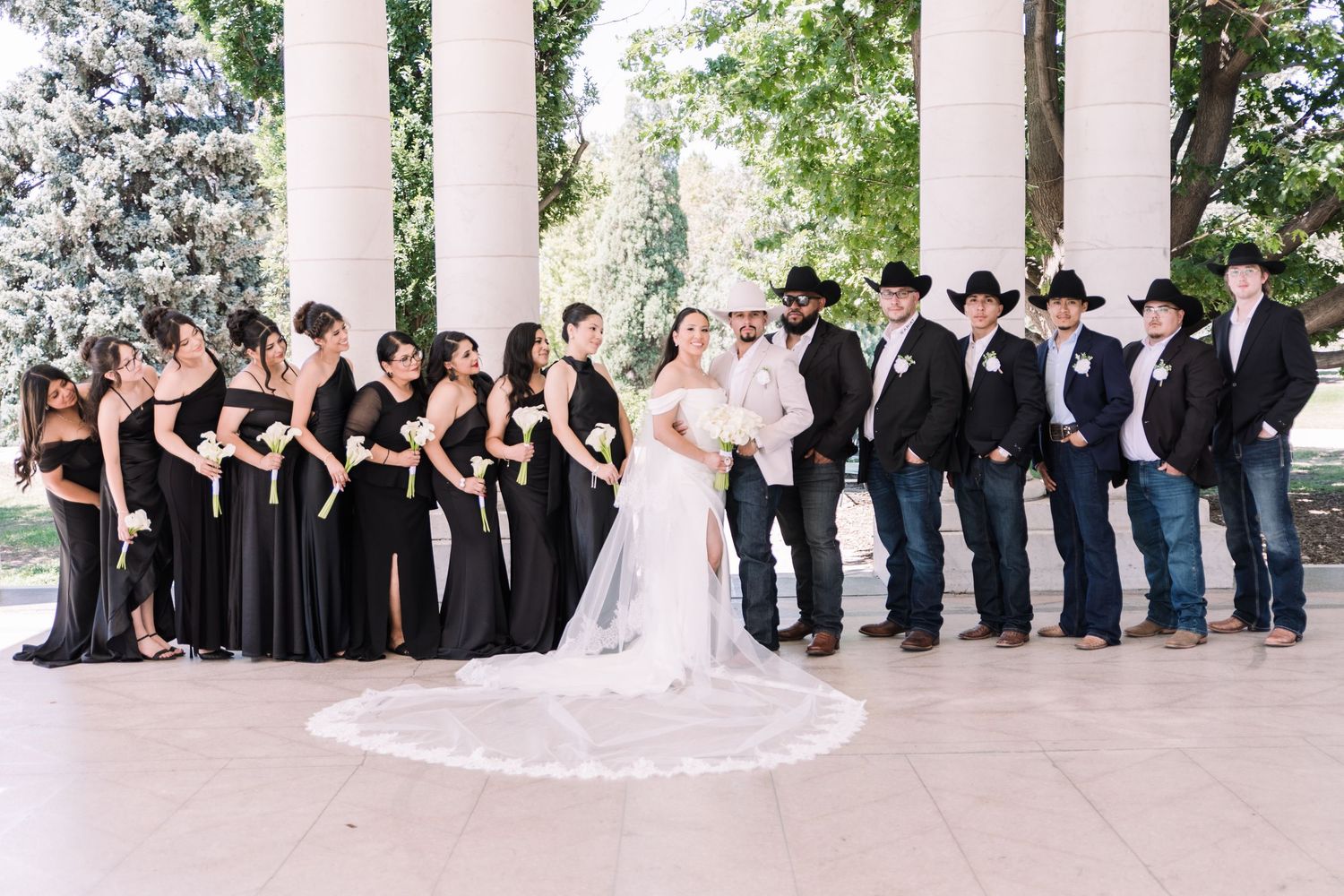 Wedding party in black attire with bride and groom, bridesmaids in black gowns and groomsmen in cowboy hats.