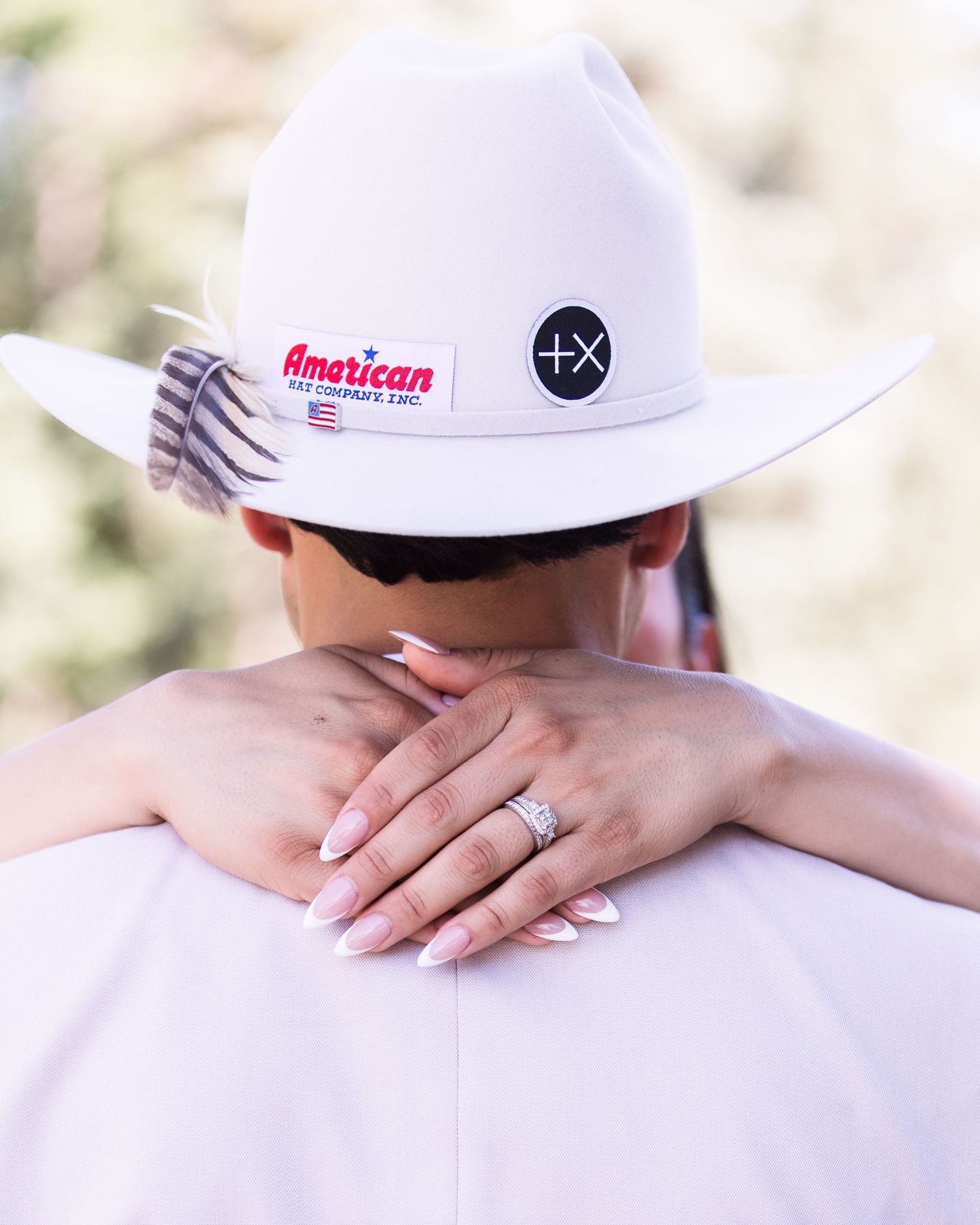 Close-up of bride's hand with diamond ring resting on groom's white cowboy hat at wedding.