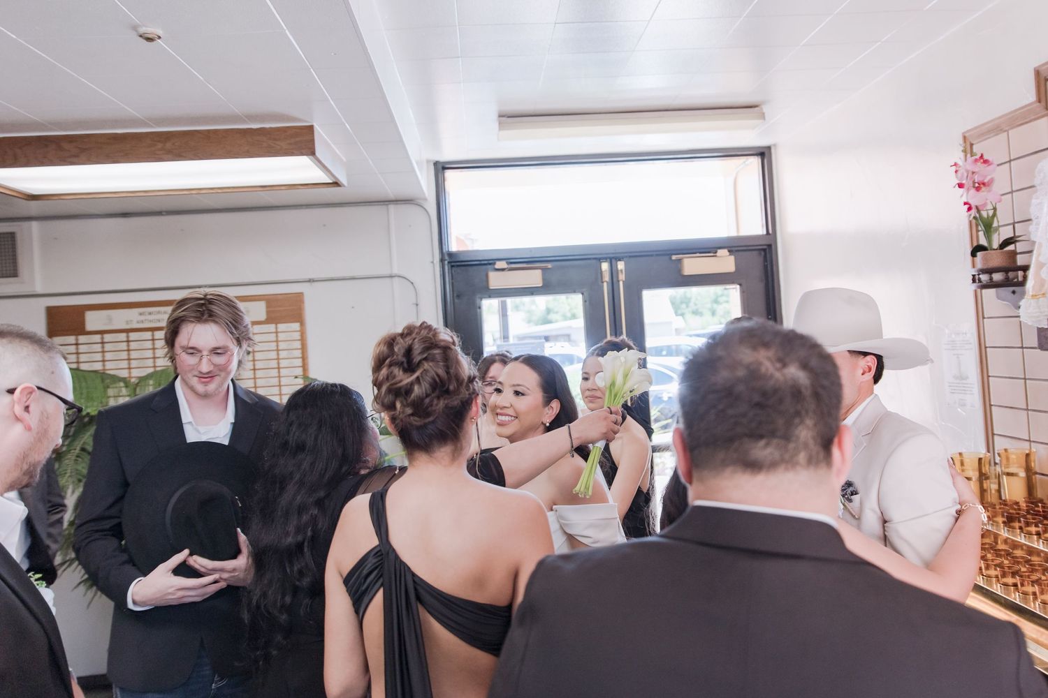 Wedding guests mingle and celebrate at reception, with groom in white cowboy hat visible in background.