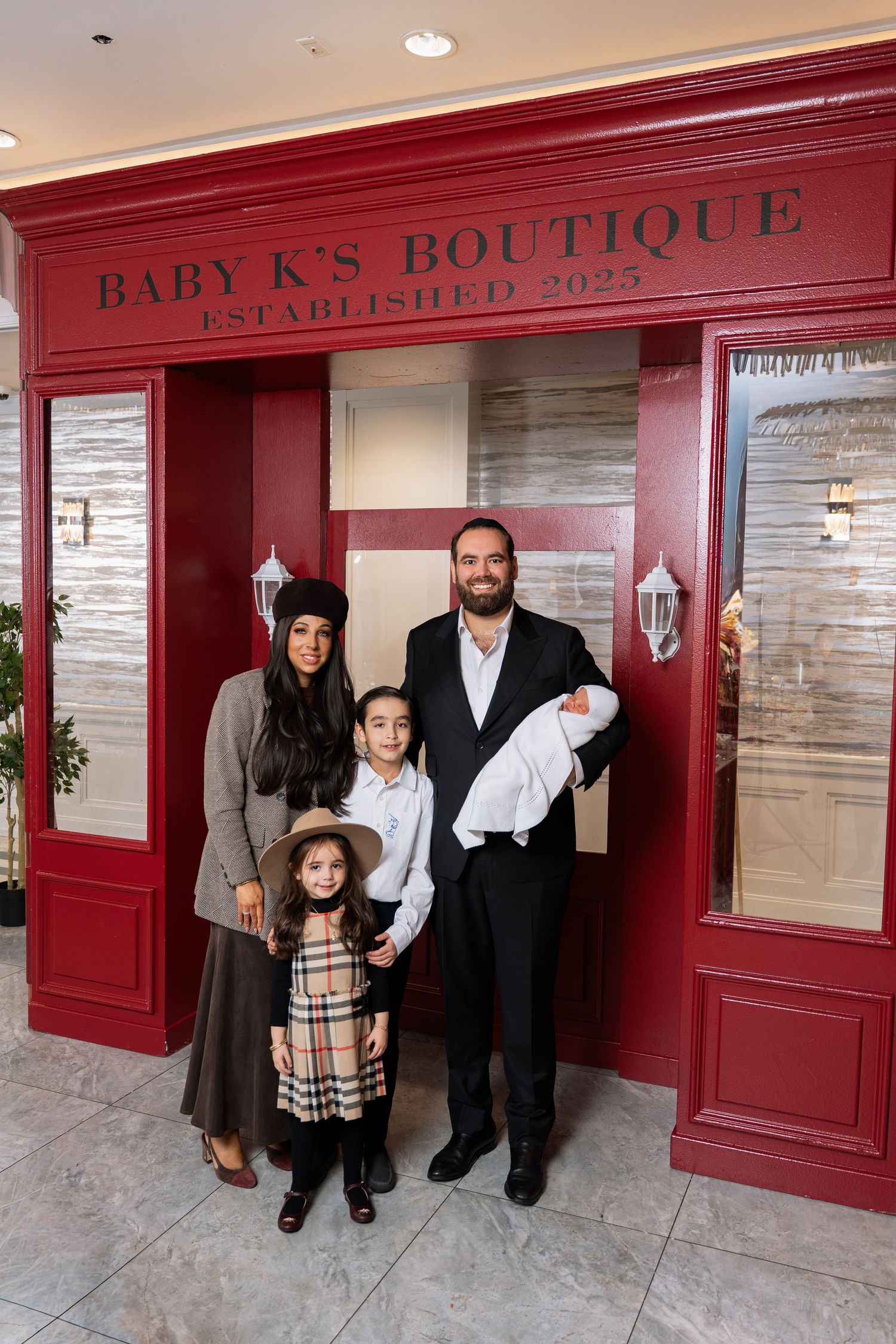 Family stands in front of Baby K's Boutique storefront with red trim and white walls.
