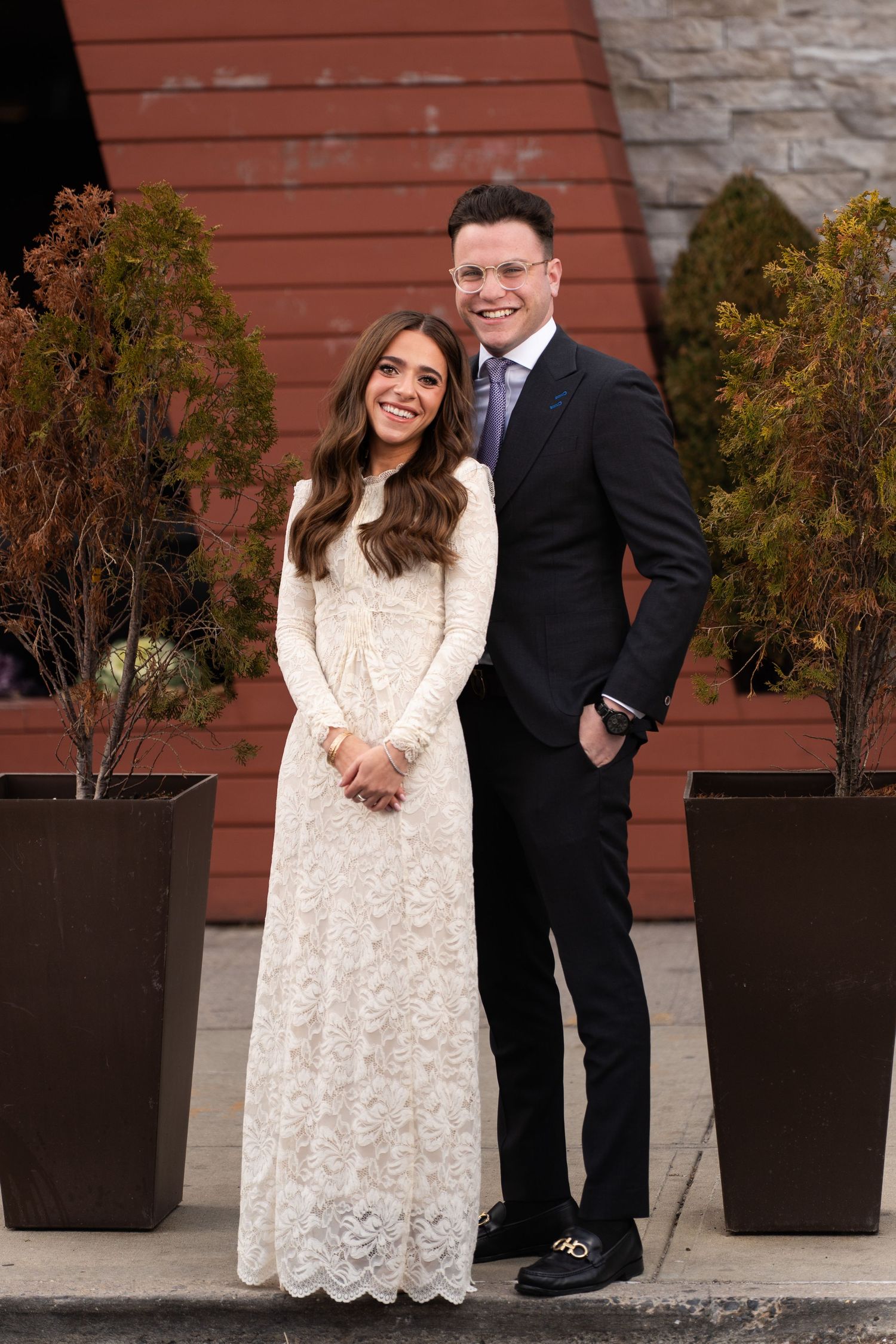 A formal portrait against a red building with decorative planters.