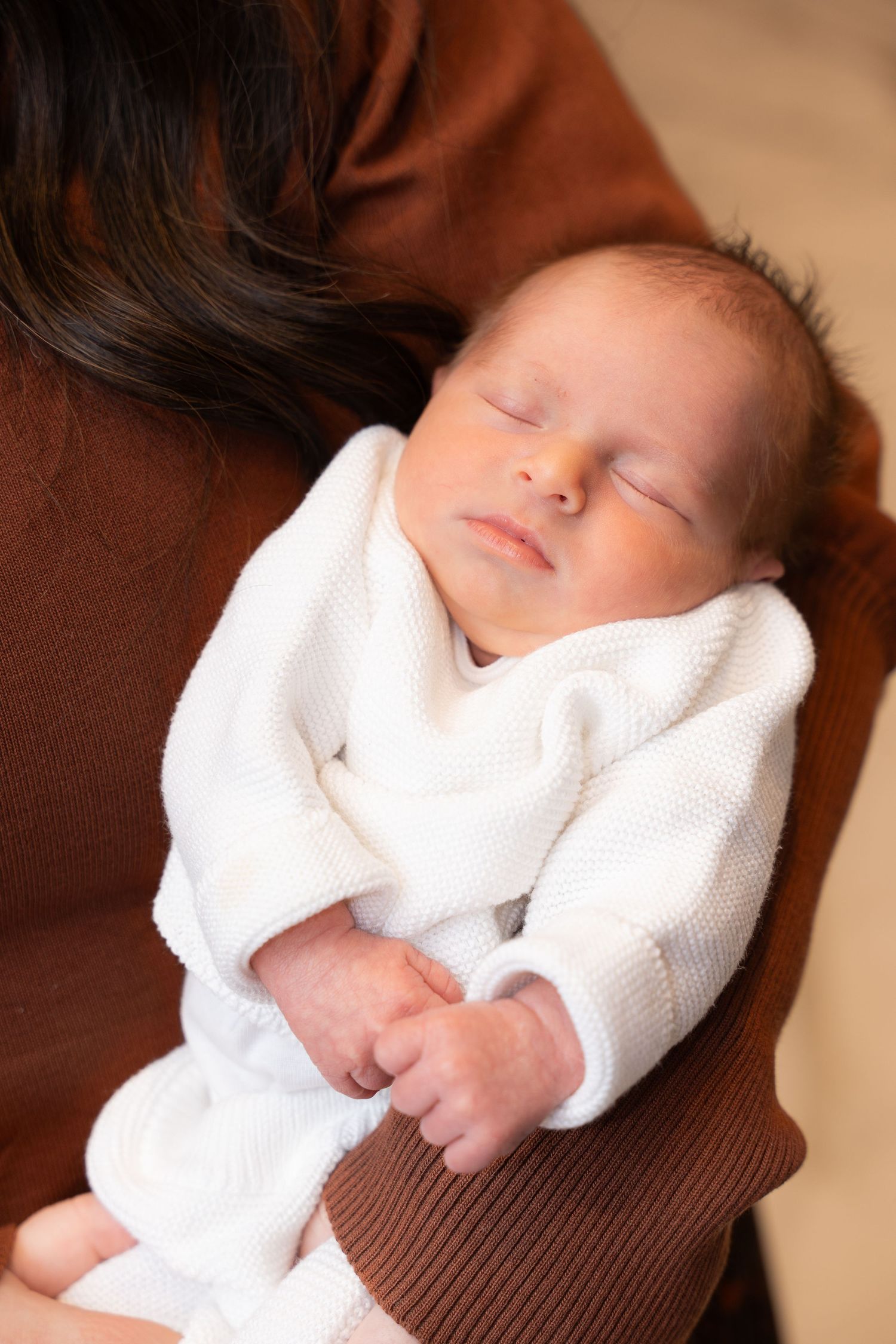 Sleeping infant wrapped in white blanket resting on brown surface.