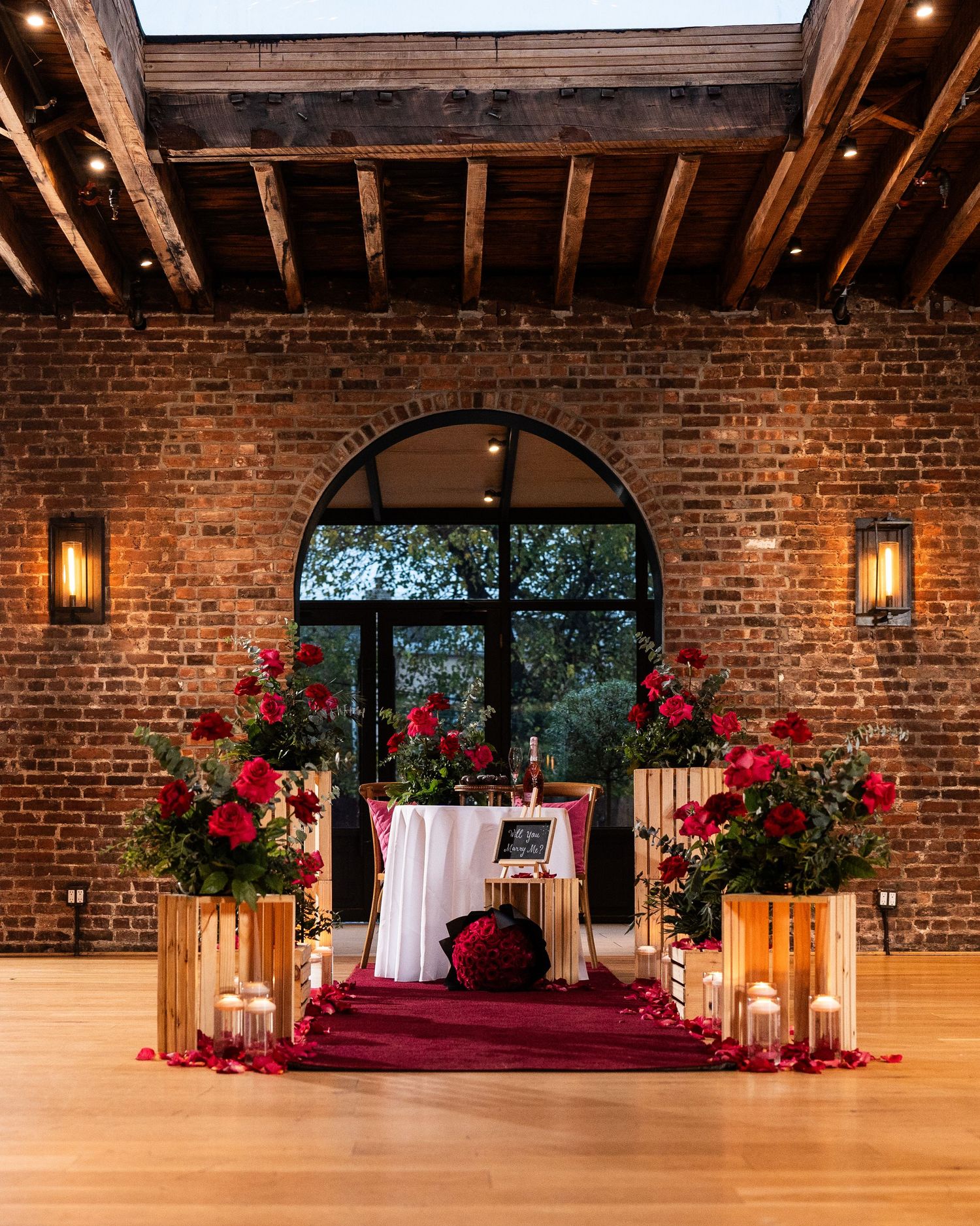 Wedding ceremony setup in brick venue with red flowers, lanterns and romantic lighting.