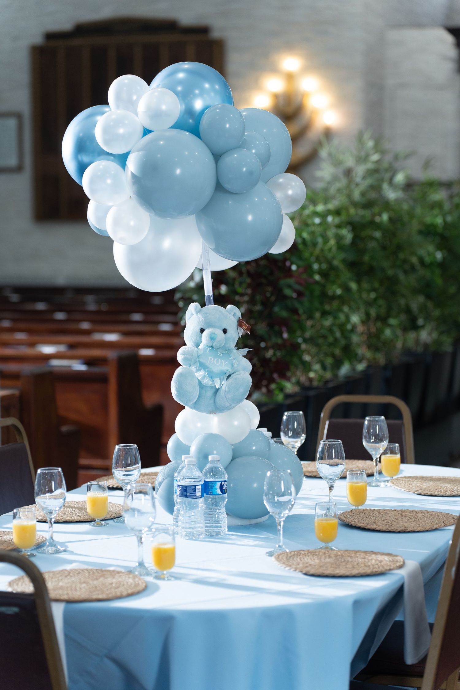 Blue and white balloon centerpieces decorate an elegant table setting with wine glasses and orange juice for a baby shower.