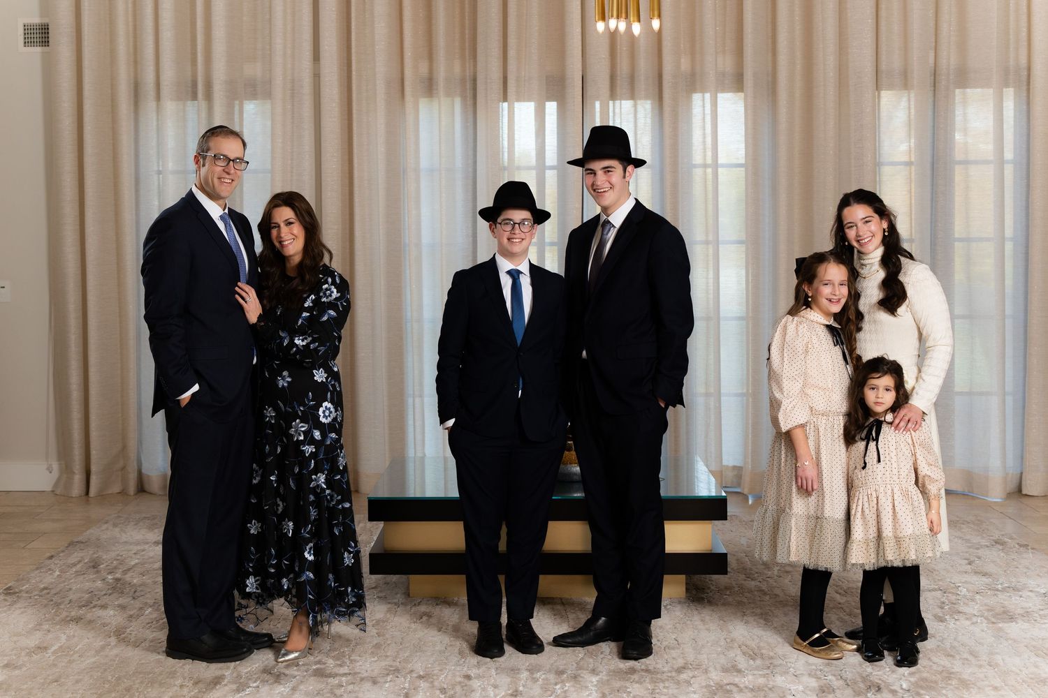 A formal family portrait of seven people in elegant attire standing together in front of light curtains.