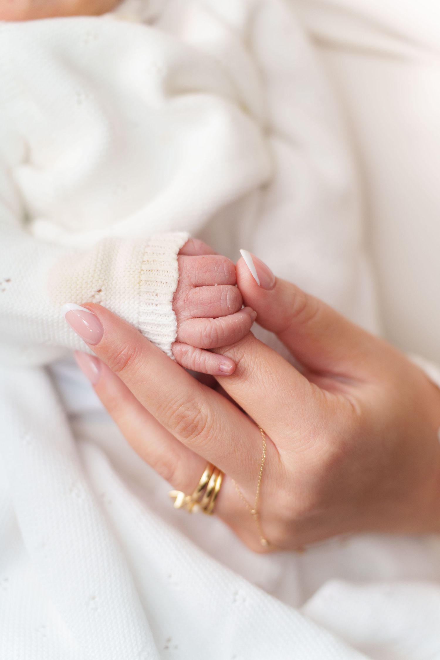 A close-up series of hands holding and caressing a small newborn baby's hand against a soft white blanket background.