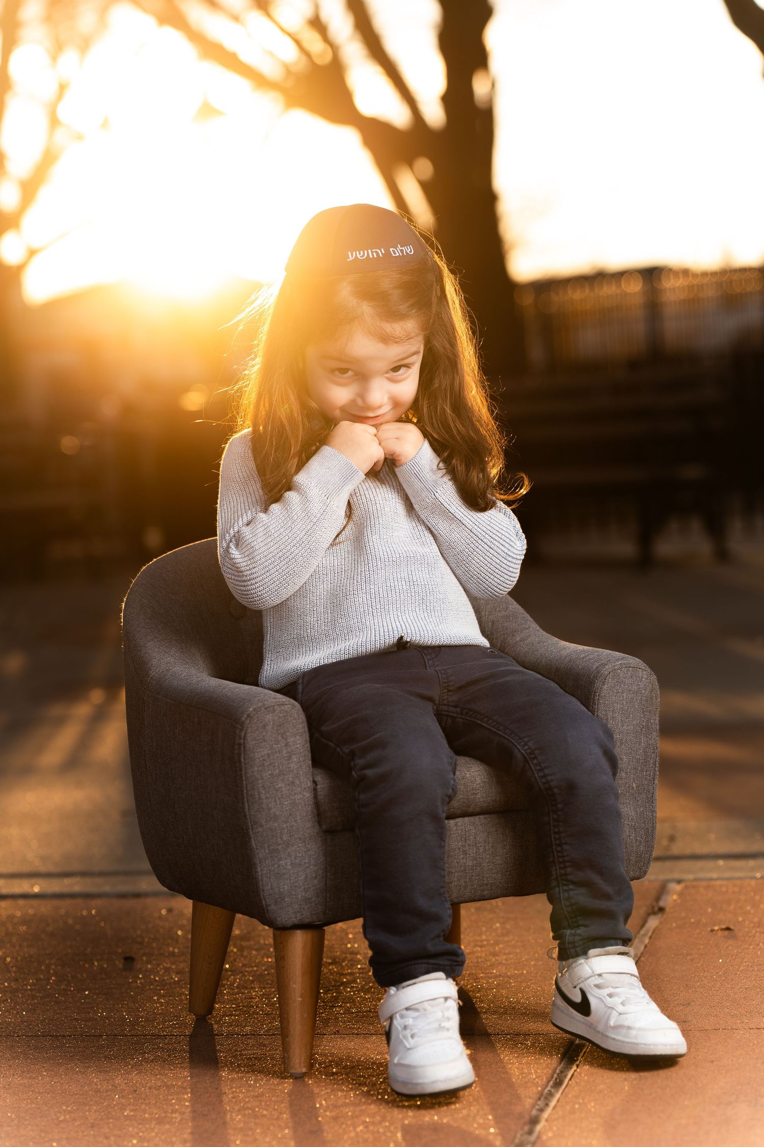 A child sitting in a dark gray armchair during golden hour outdoors.