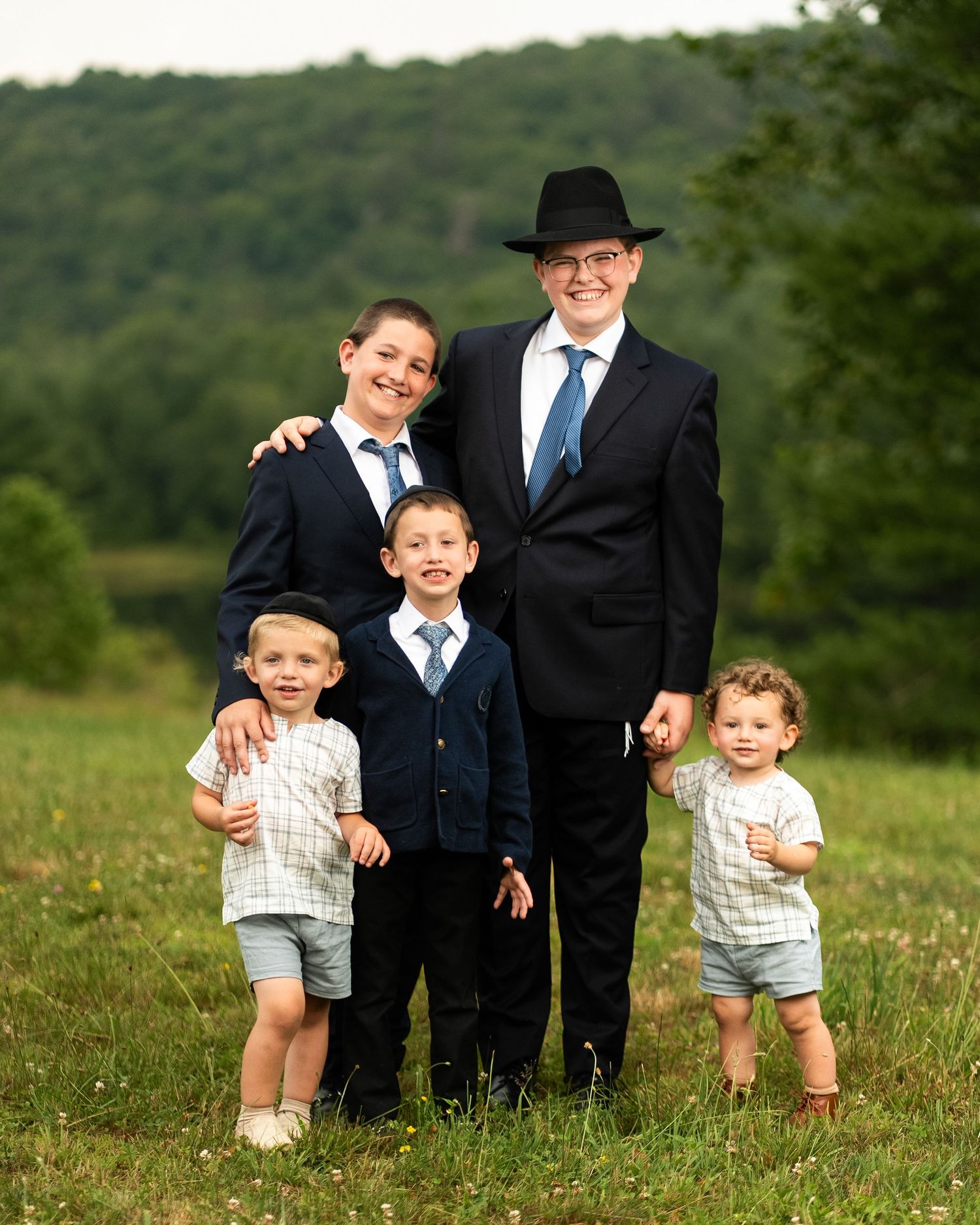 A formal family portrait outdoors with four people in traditional dress against a green hillside background.