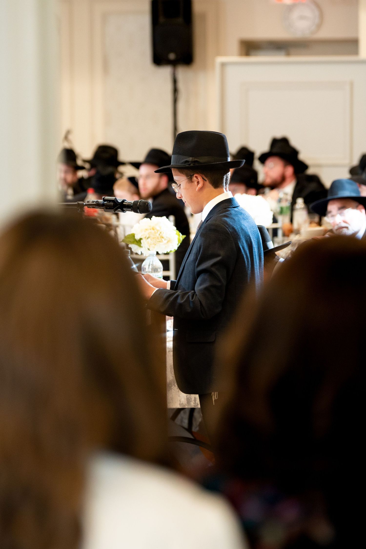 Crowd scene at indoor event with people wearing black hats and formal attire.