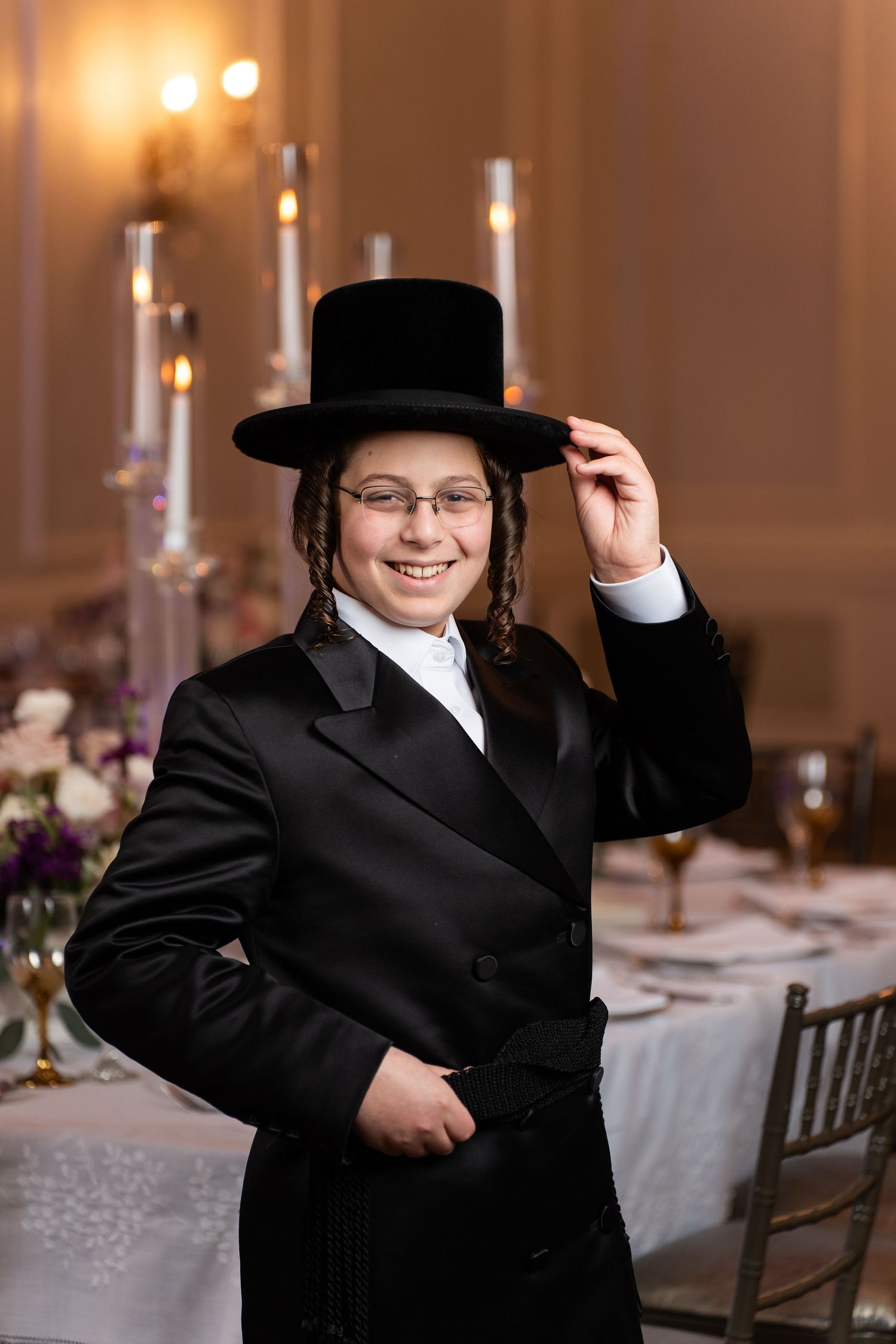 Young child in formal black suit and hat poses in multiple candid shots at an elegant reception venue.