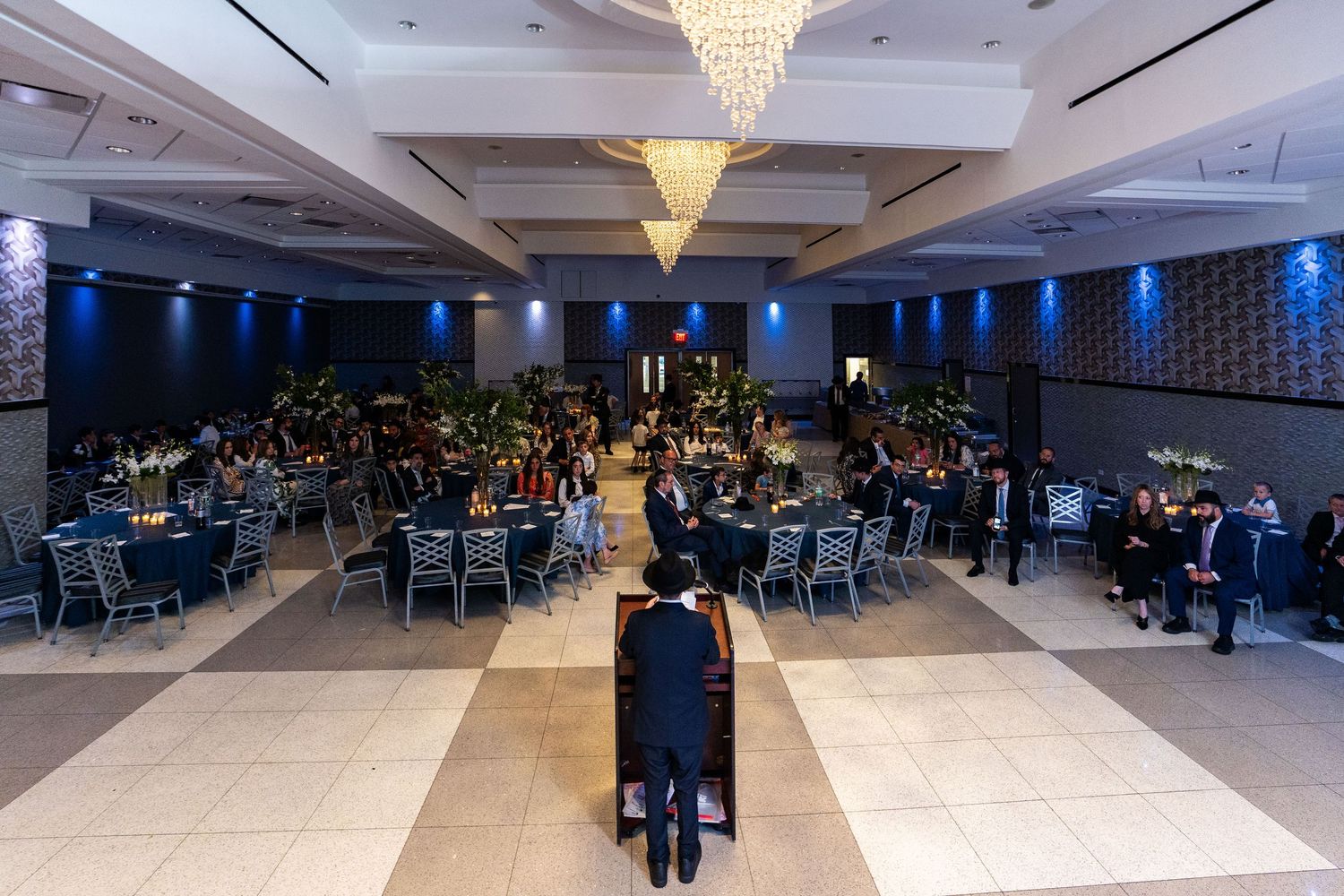 Large elegant ballroom with crystal chandeliers and blue accent lighting set up for a formal event.