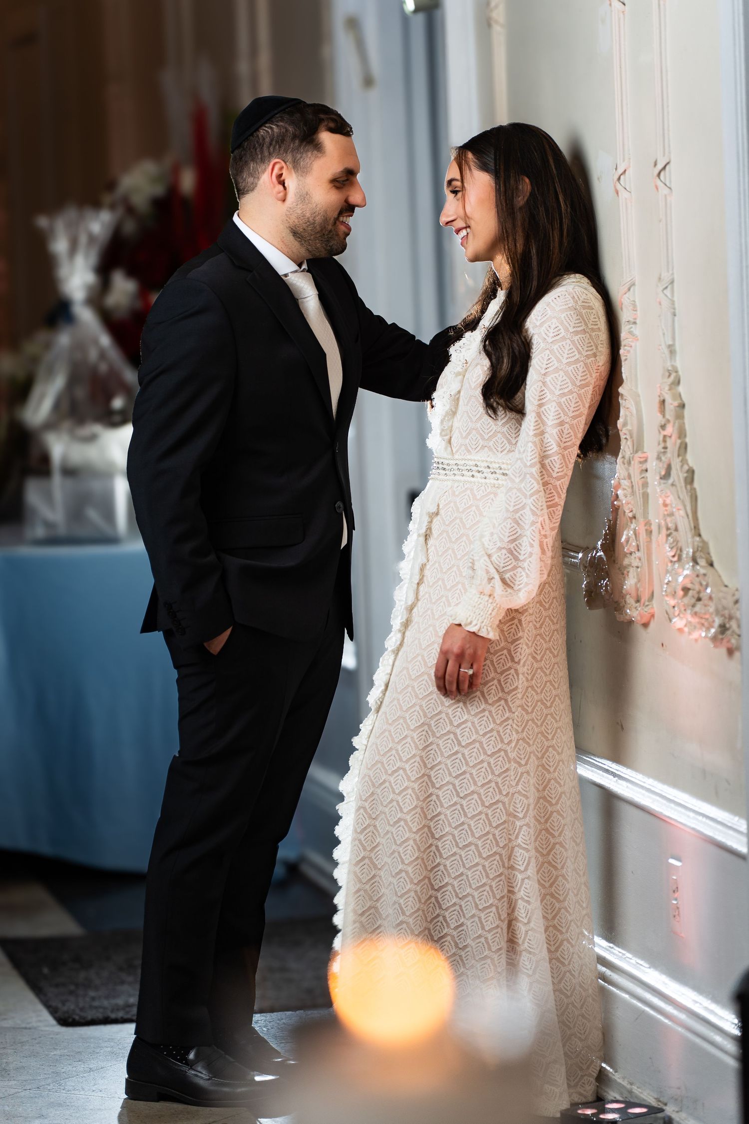 Romantic moment between bride and groom in white dress and black suit against an indoor backdrop.