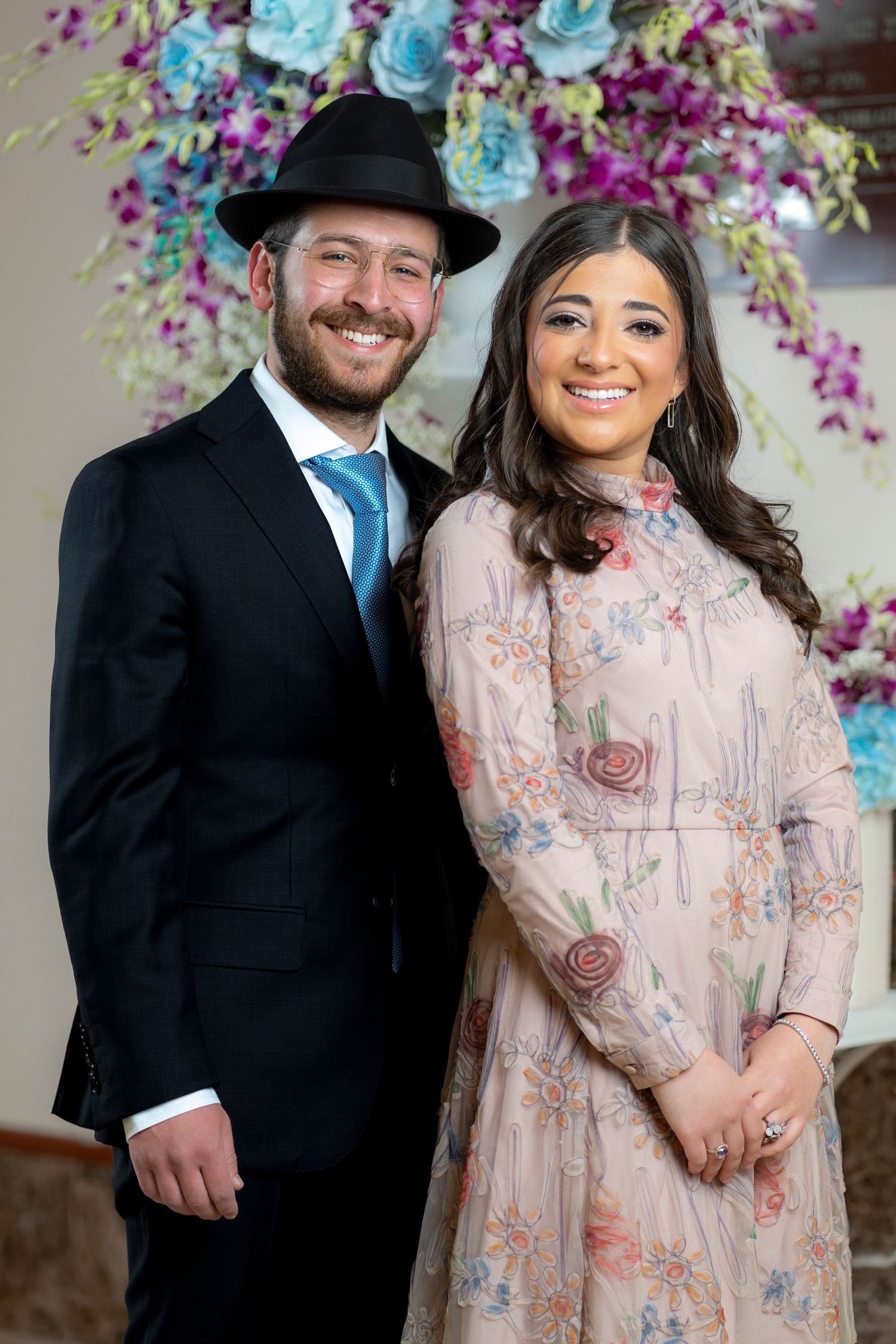 Engagement photos with couple in formal attire against colorful floral arch backdrop.