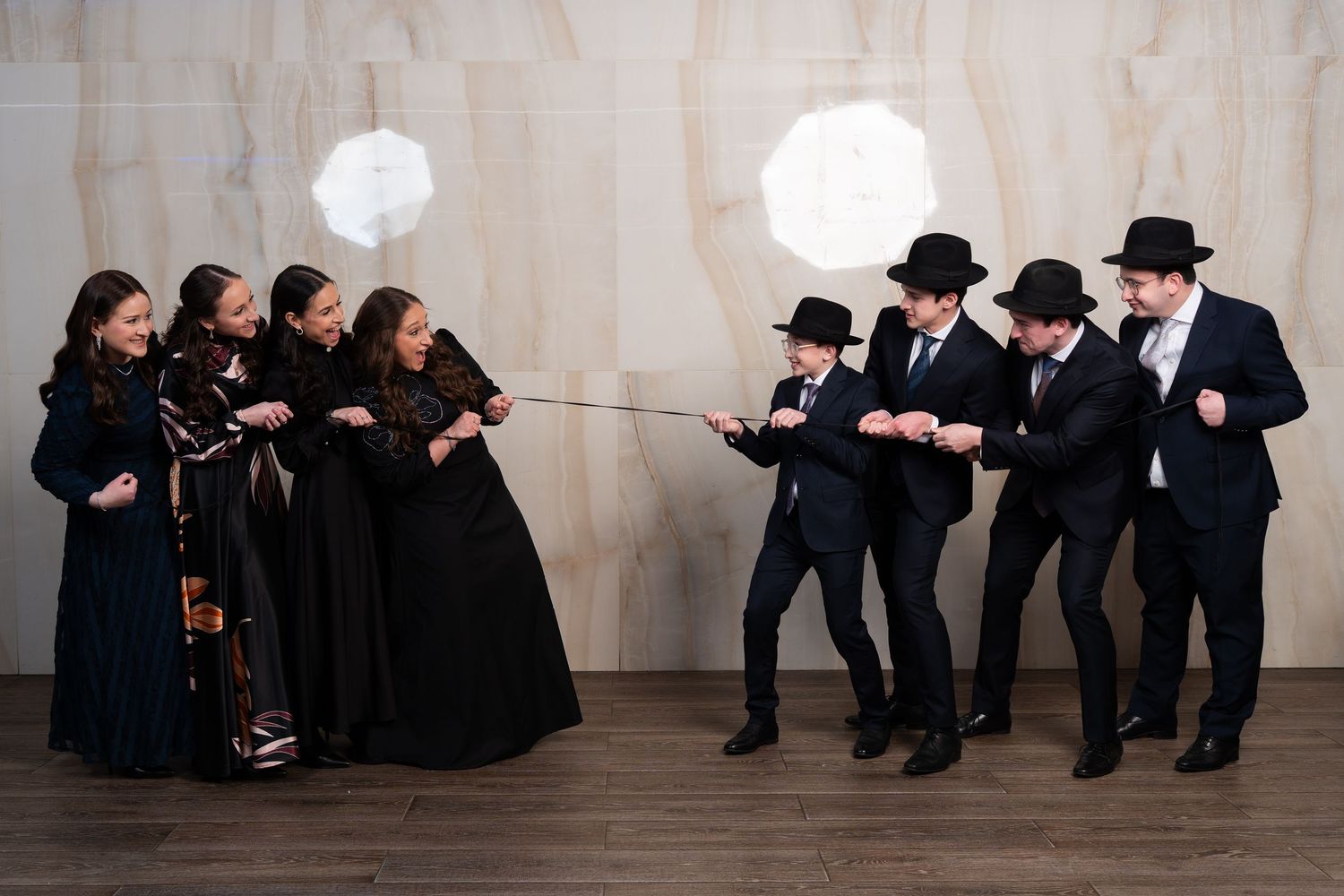 A group of people in black attire sit against a white wall in a choreographed performance sequence.