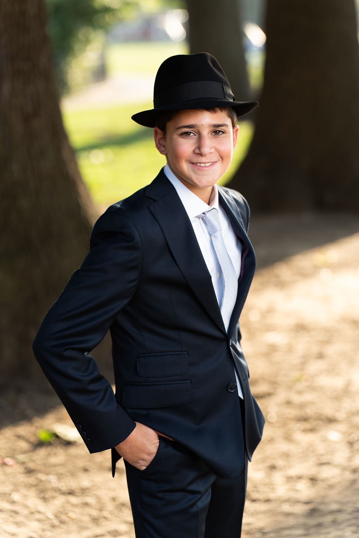A series of four photos showing someone in a formal black suit and hat posing outdoors in a natural setting.