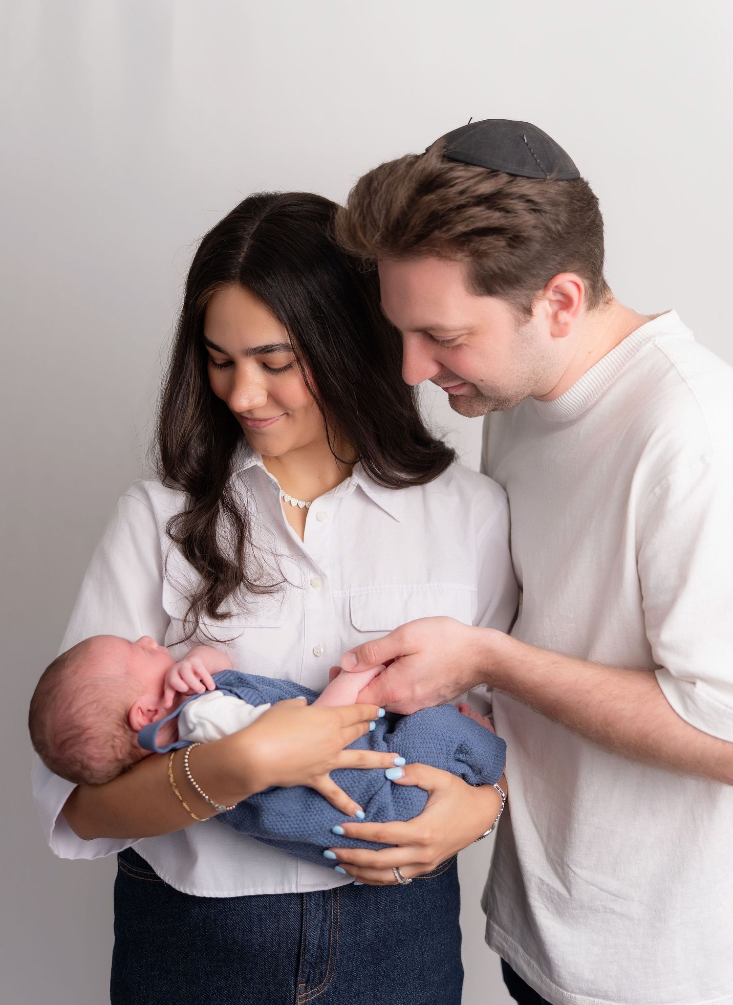 A couple in white shirts lovingly gazes at their newborn baby wrapped in a blue blanket.