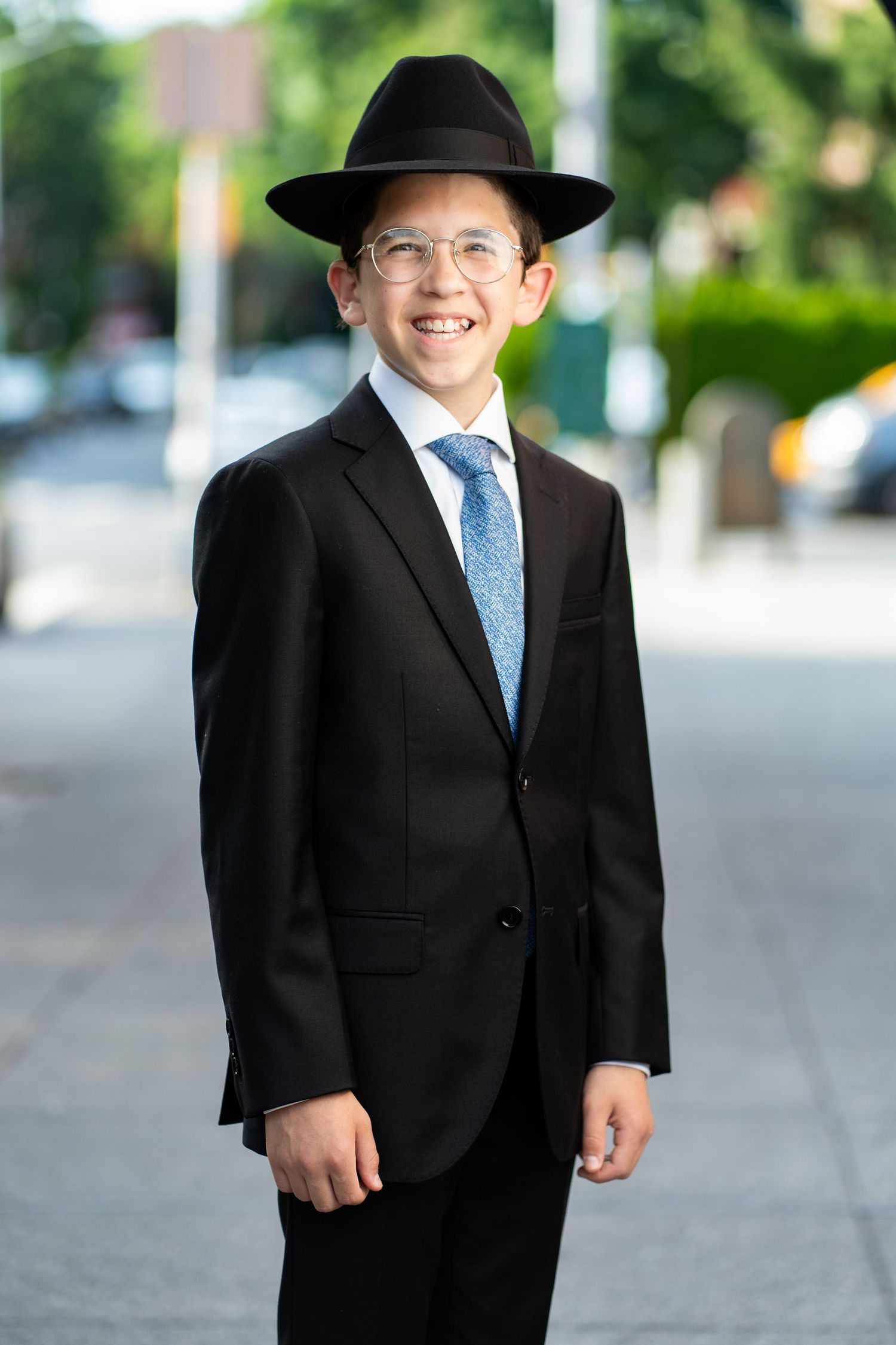 Person in formal black suit and blue tie walking on city sidewalk.