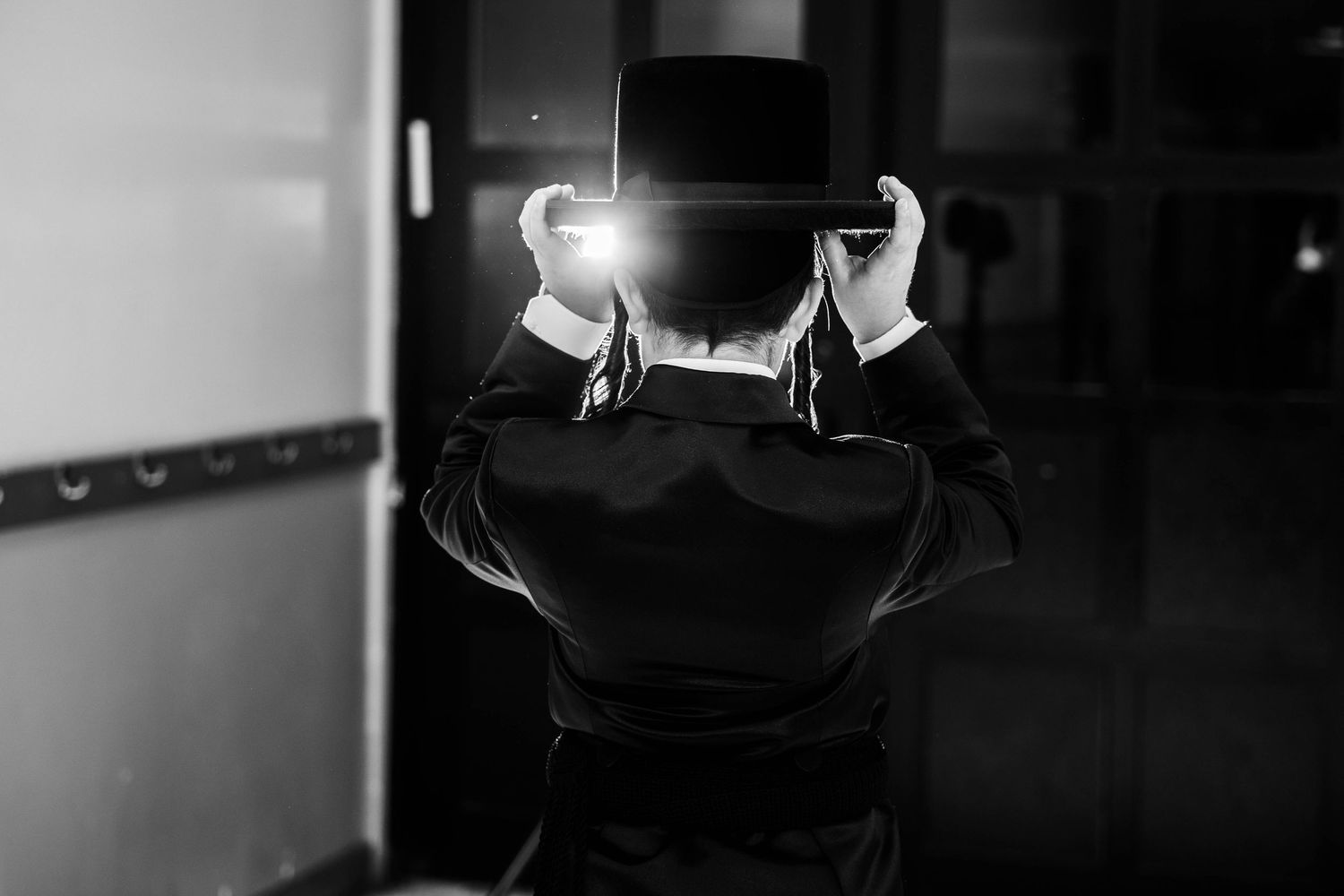 A black and white photograph of someone adjusting their hat from behind.