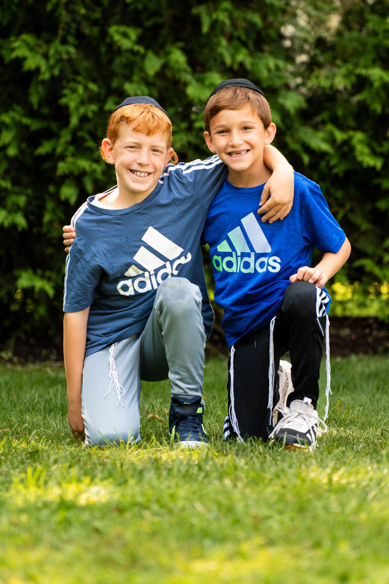 Children sitting together in grass wearing Adidas sportswear and casual clothing outdoors.