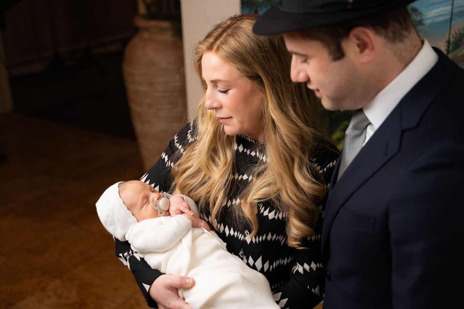 A couple holds their newborn baby in a series of intimate indoor portraits with warm lighting.