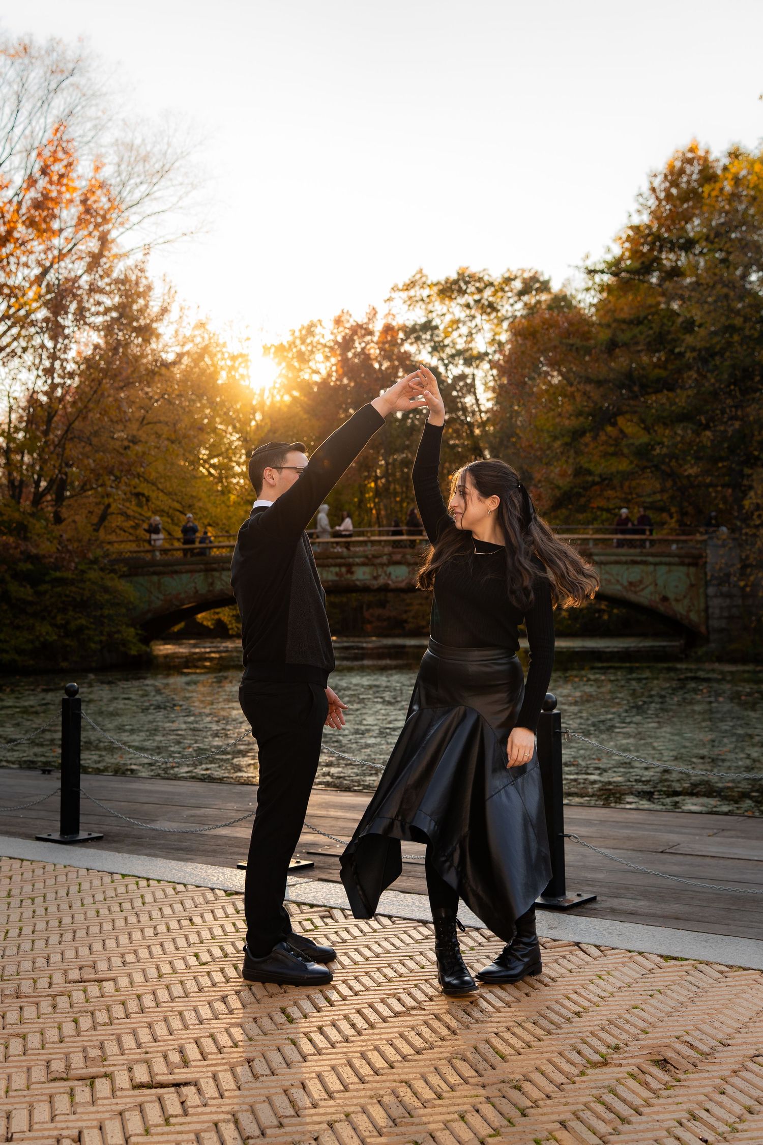 Couple dancing at sunset by a lake in Central Park, NYC, wearing elegant black outfits during autumn.