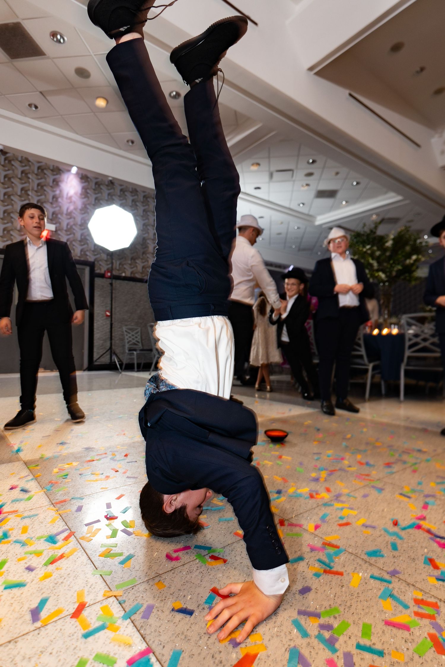 Man in suit doing a handstand on confetti-covered dance floor at a celebration event.